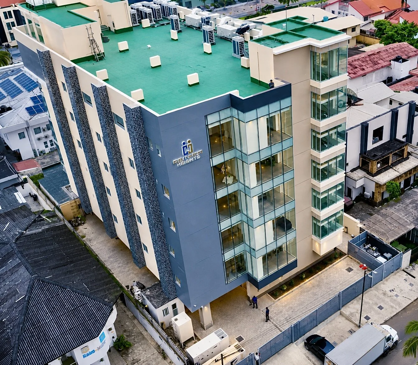 Aerial view of a modern multi-story cedarcrest hospital building with a green rooftop, glass balconies, and the sign 'Cedarcrest Hospital' on the side, surrounded by smaller residential and commercial buildings.
