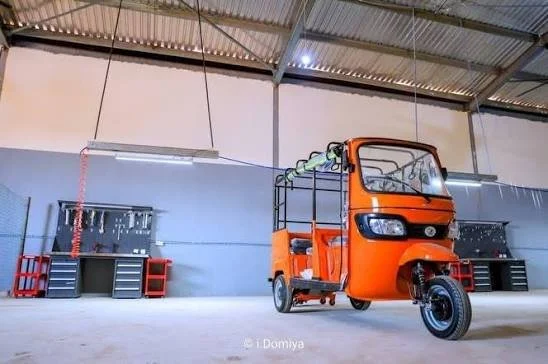 Orange three-wheeled utility vehicle with open cargo area parked inside a warehouse.