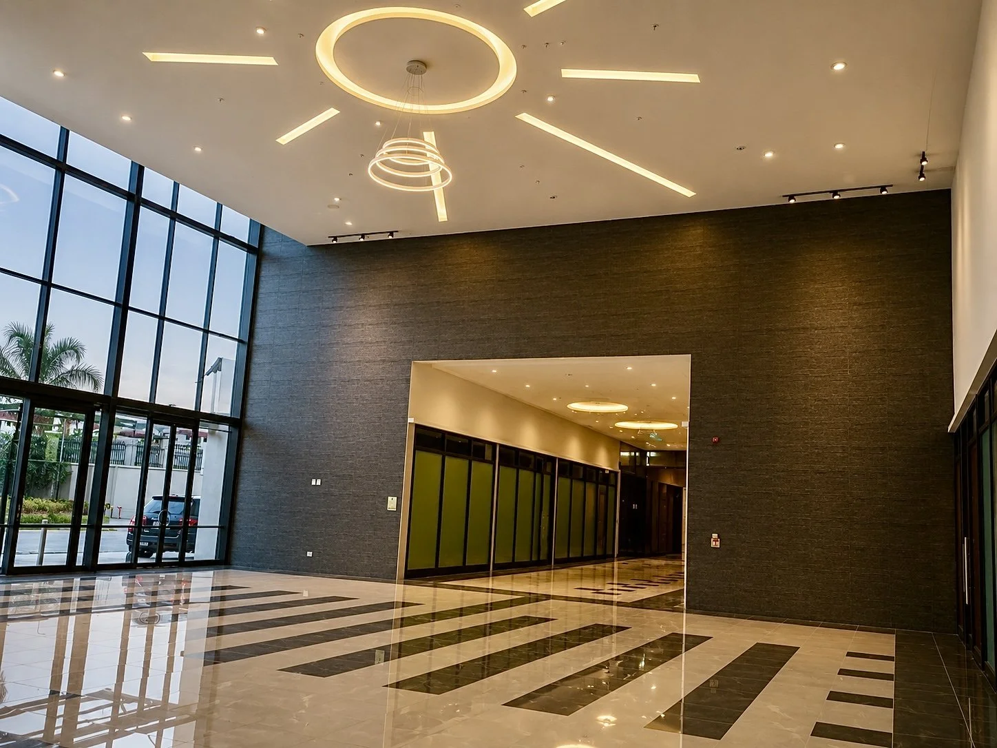Modern lobby with large glass windows, polished marble flooring with black and white pattern, dark textured wall, and stylish circular ceiling lights.