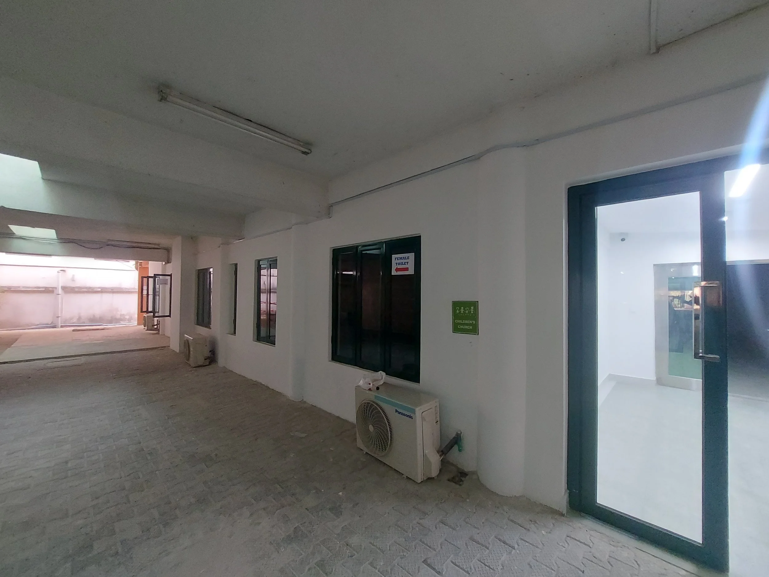 Interior of a children’s church building (RCCG Olive Branch) with white walls, tiled flooring, air conditioning units, a door with a sign, windows, and a corridor leading outside; Project Managed by IHOD.