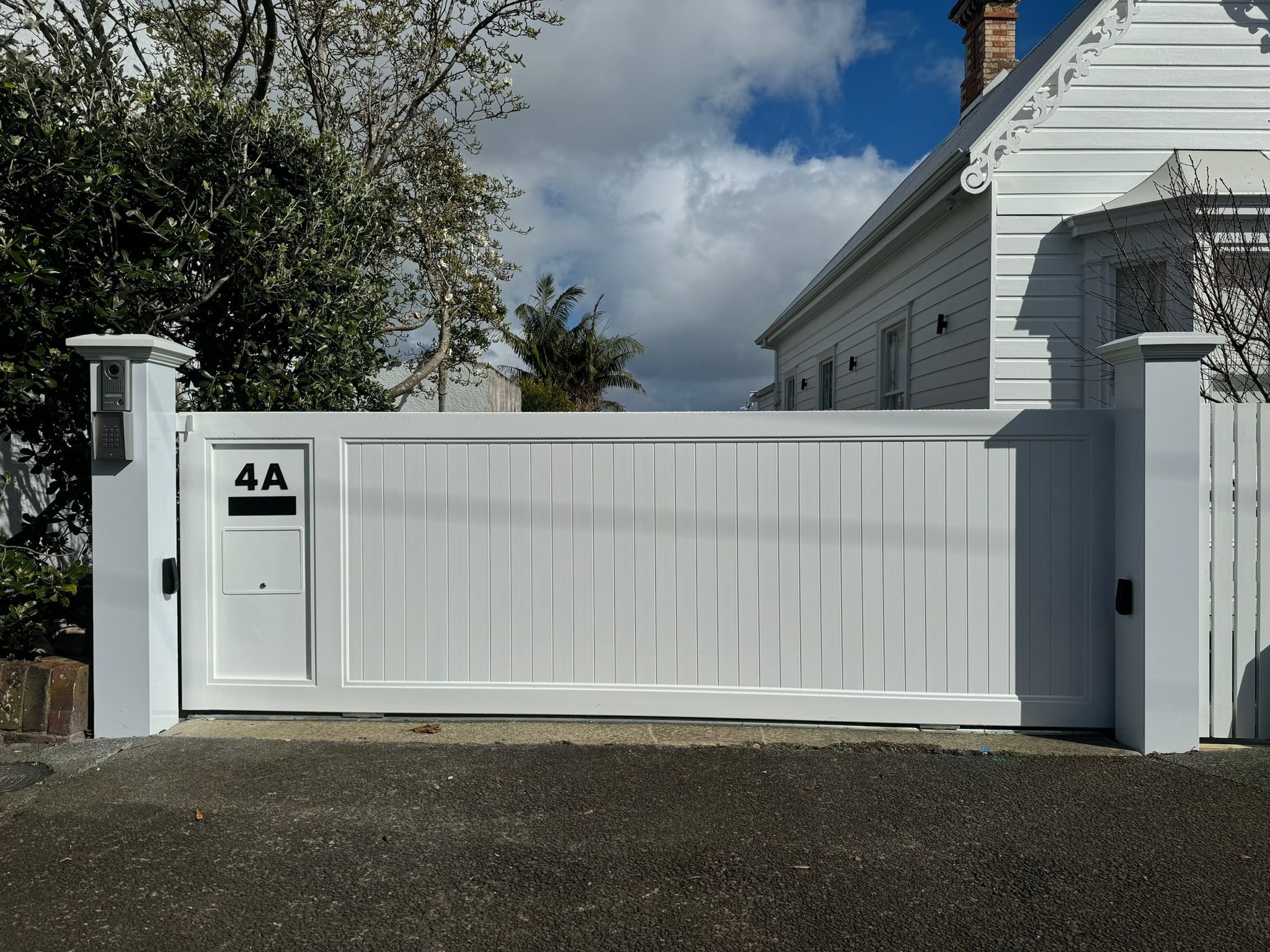 White modern fence with house and trees behind, cloudy sky overhead.