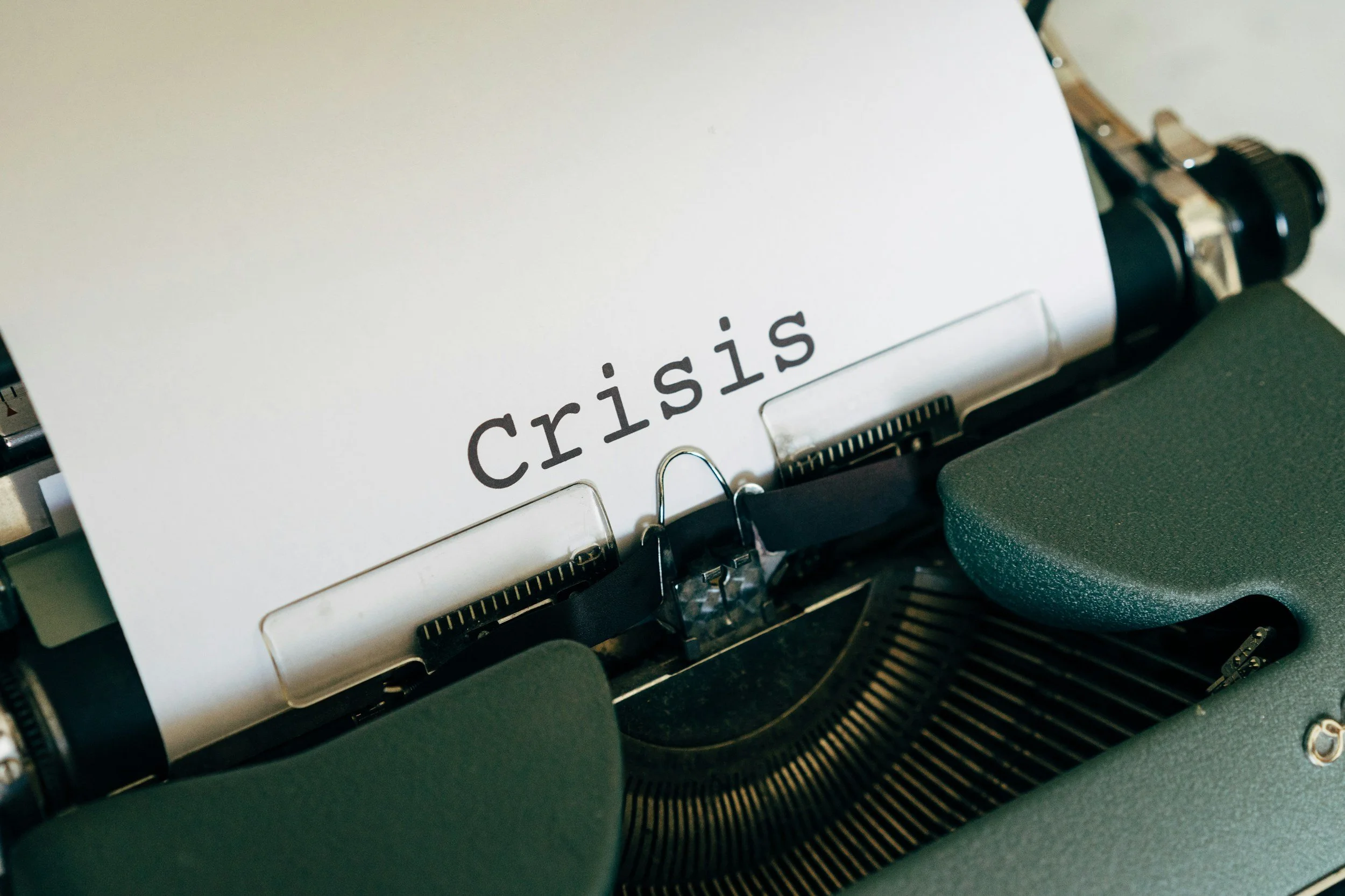 Close-up of a vintage typewriter with a sheet of paper inserted that has the word 'crisis' typed on it.