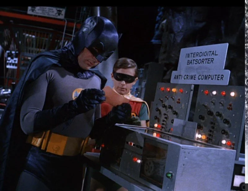 Batman and Robin in costume examining a computer control panel labeled 'Interdigital Batsorter' and 'Anti-Crime Computer' on a set or lab.