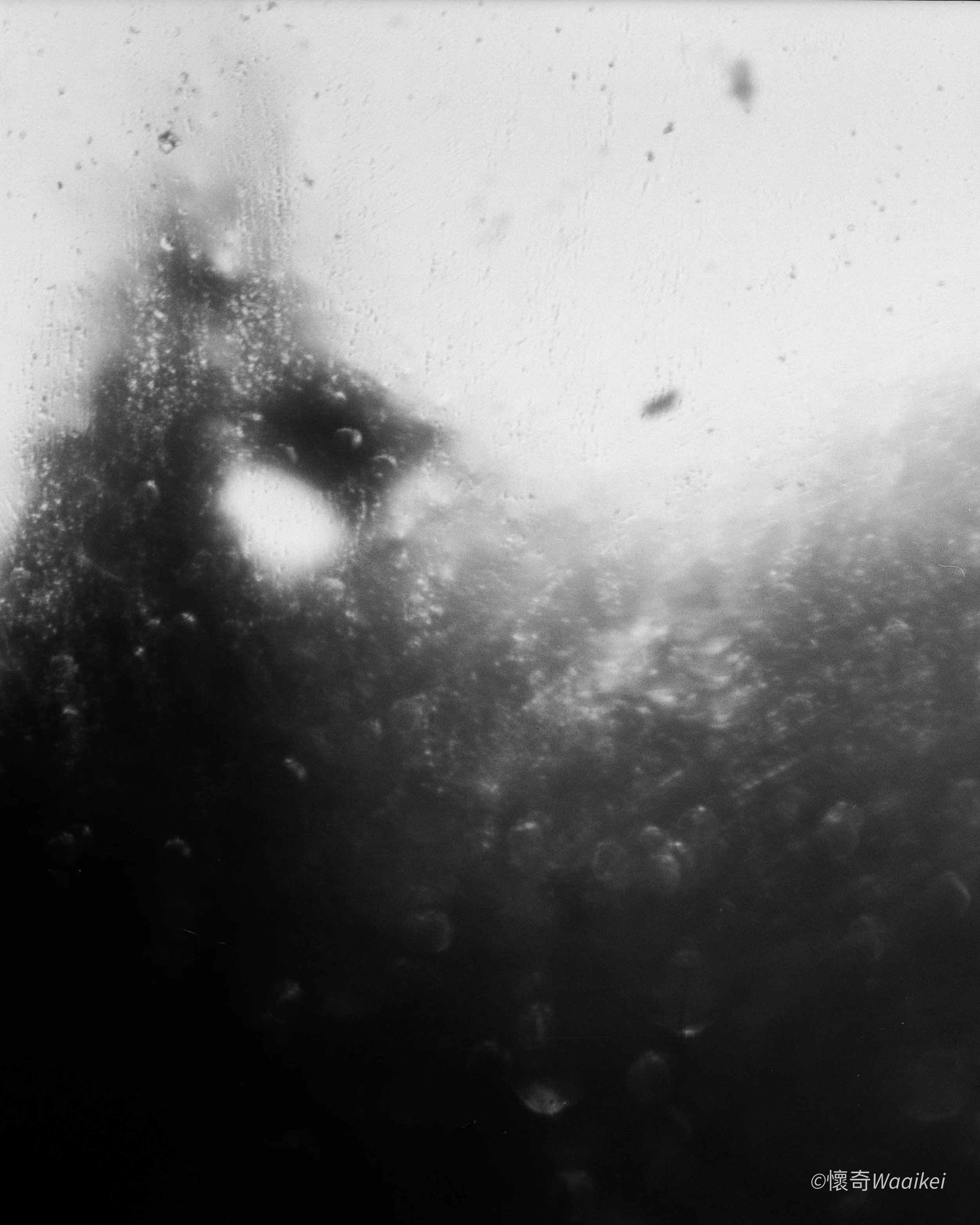 View of the moon's surface through a glass with water droplets, showing the textured terrain and craters of the moon in black and white.