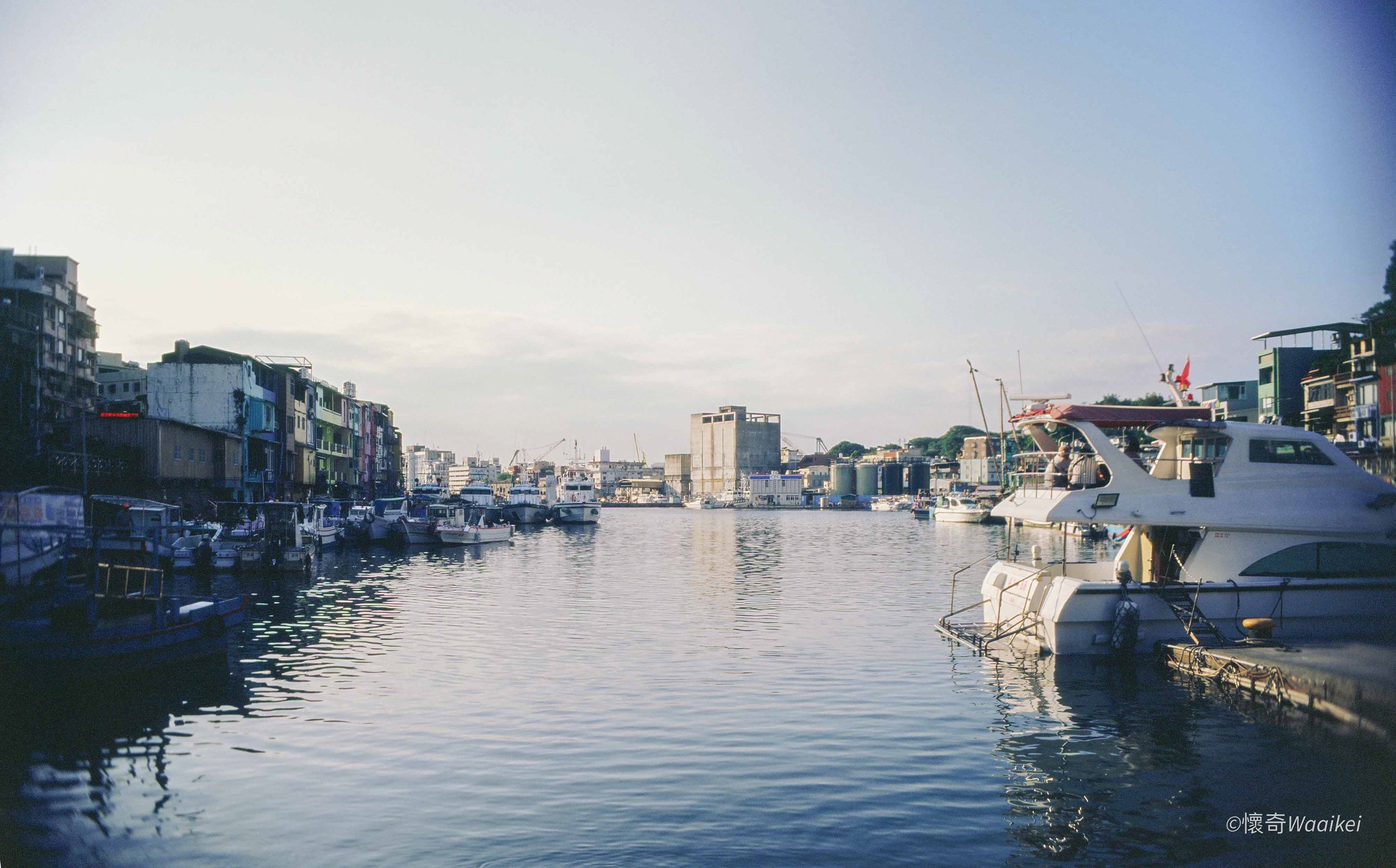A marina with several docked boats and colorful buildings along the waterfront, under a blue sky.