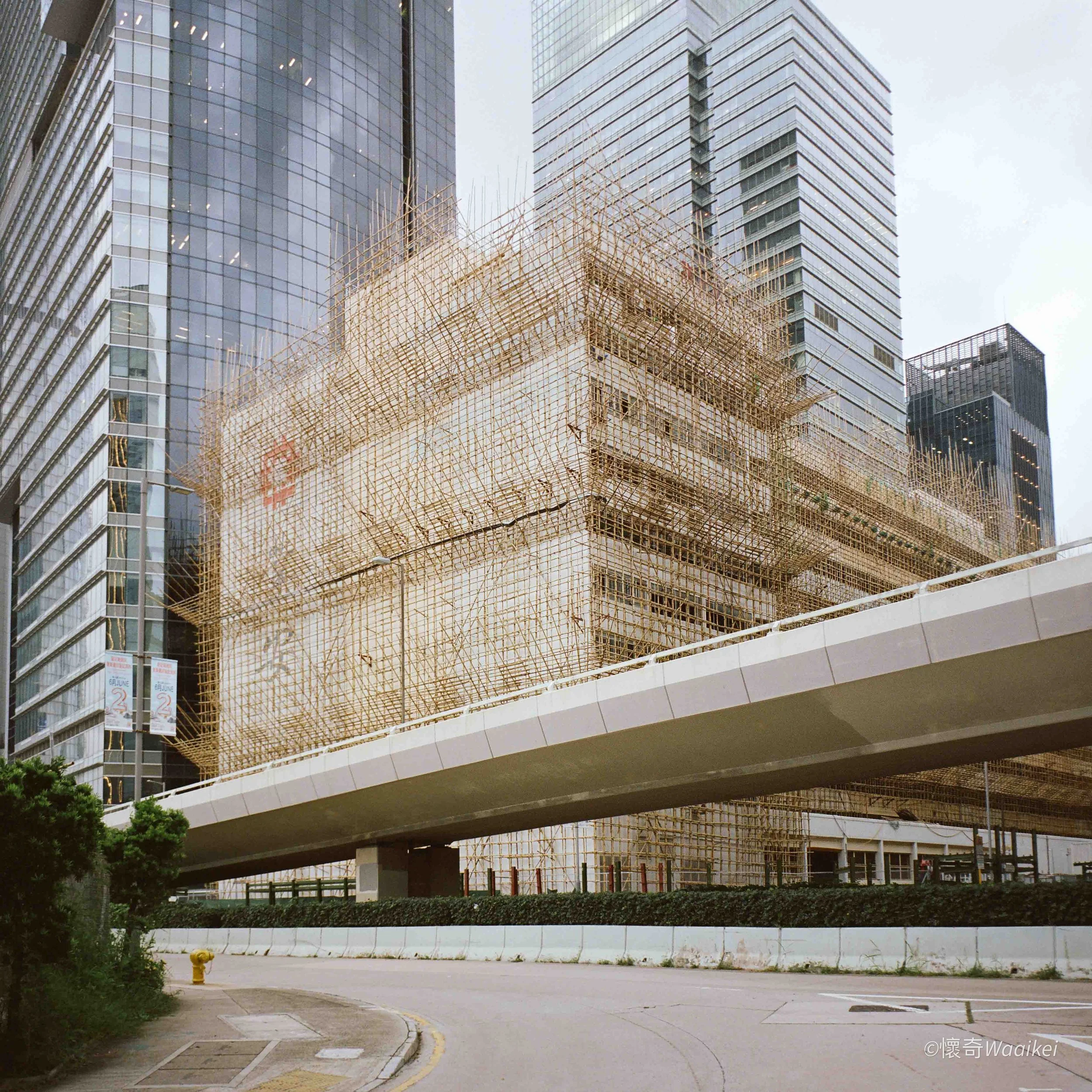View of tall glass buildings in an urban area with a construction scaffold in the foreground and a curved road below.