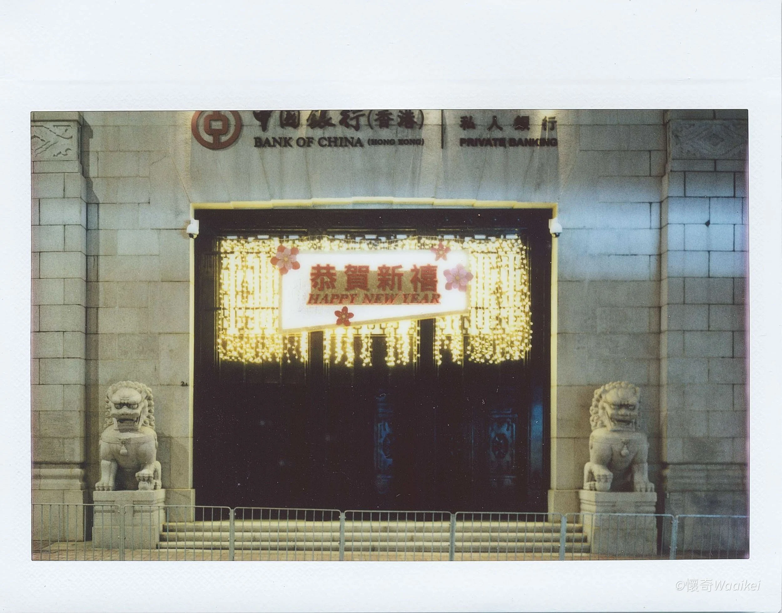 Entrance to a building with Asian architectural elements, featuring two stone lion statues at the doorway, illuminated signs, and decorative lighting and flowers celebrating the New Year.