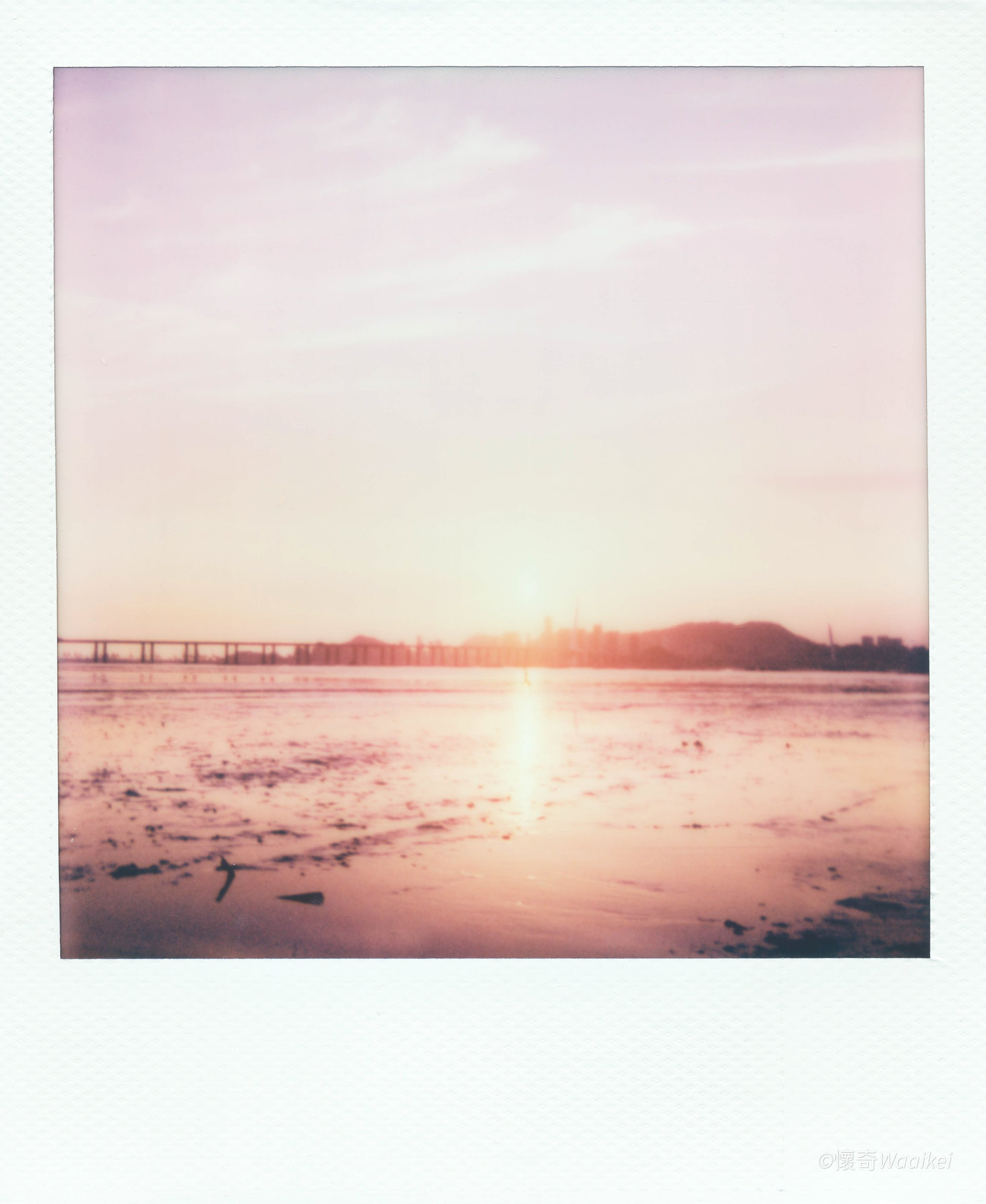 Sunset over a body of water with a bridge in the distance and a clear sky.