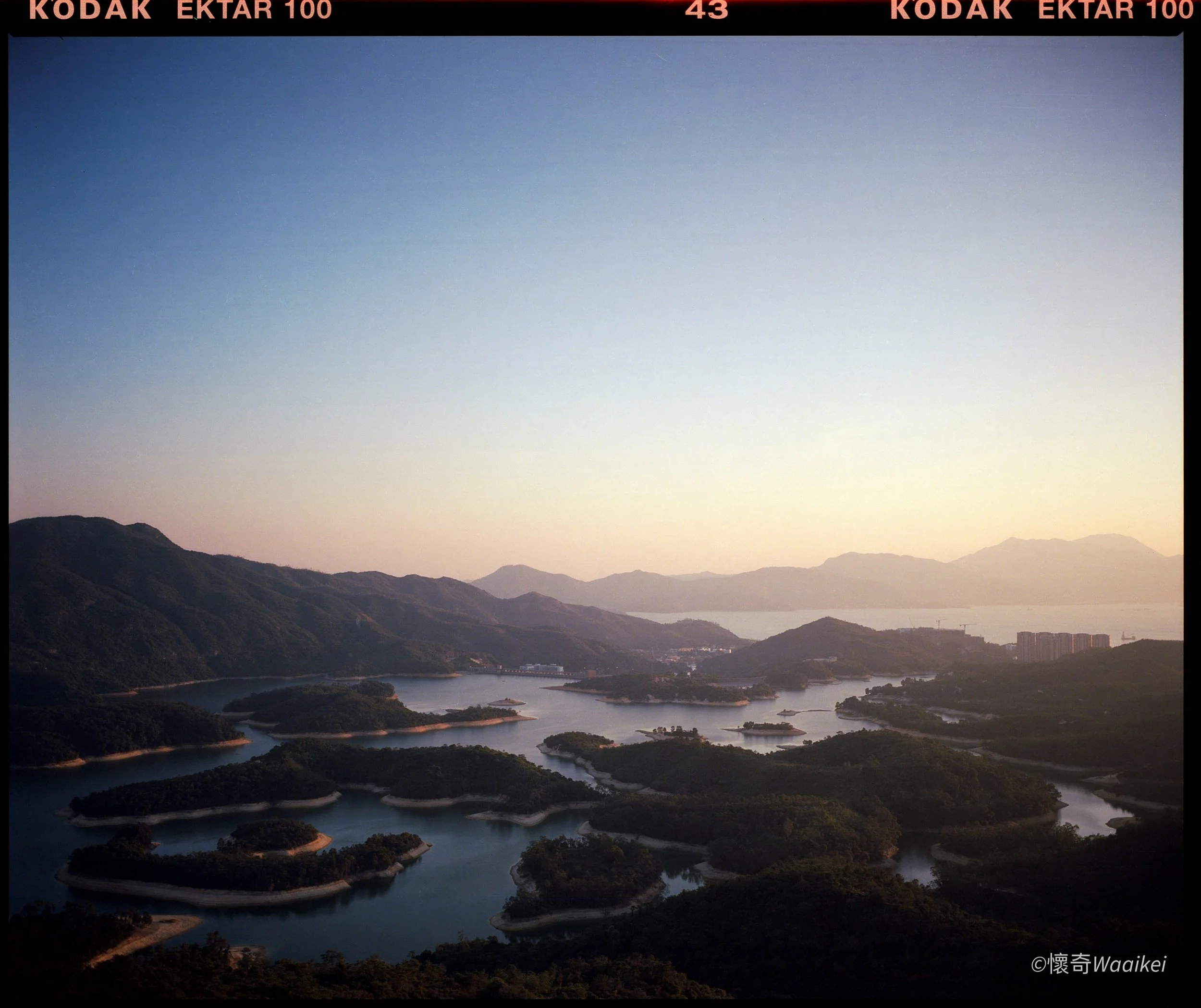 Scenic view of a large river with multiple inlets and islands, surrounded by green mountains and hills under a clear blue sky.
