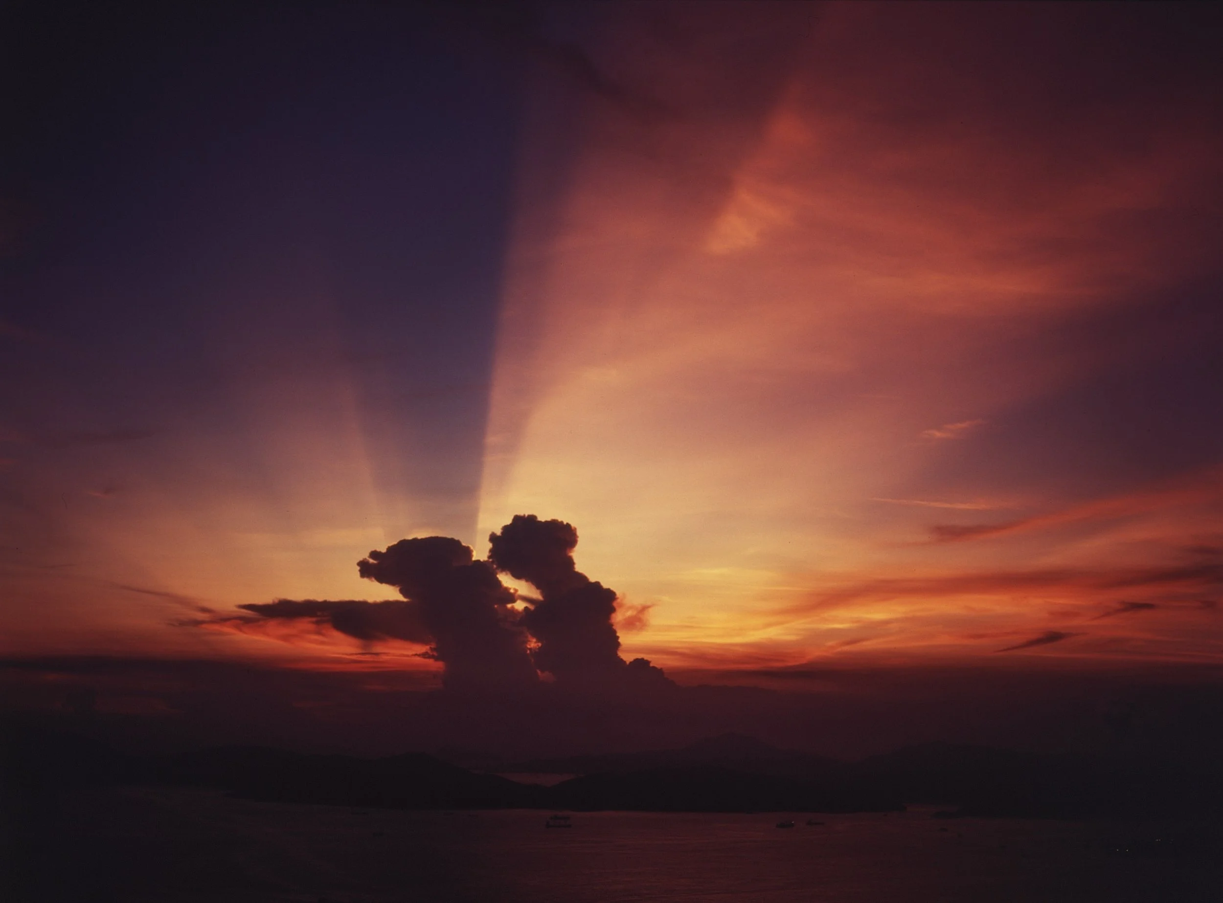 Sunset over mountains with dark clouds and colorful sky in shades of orange, pink, and purple