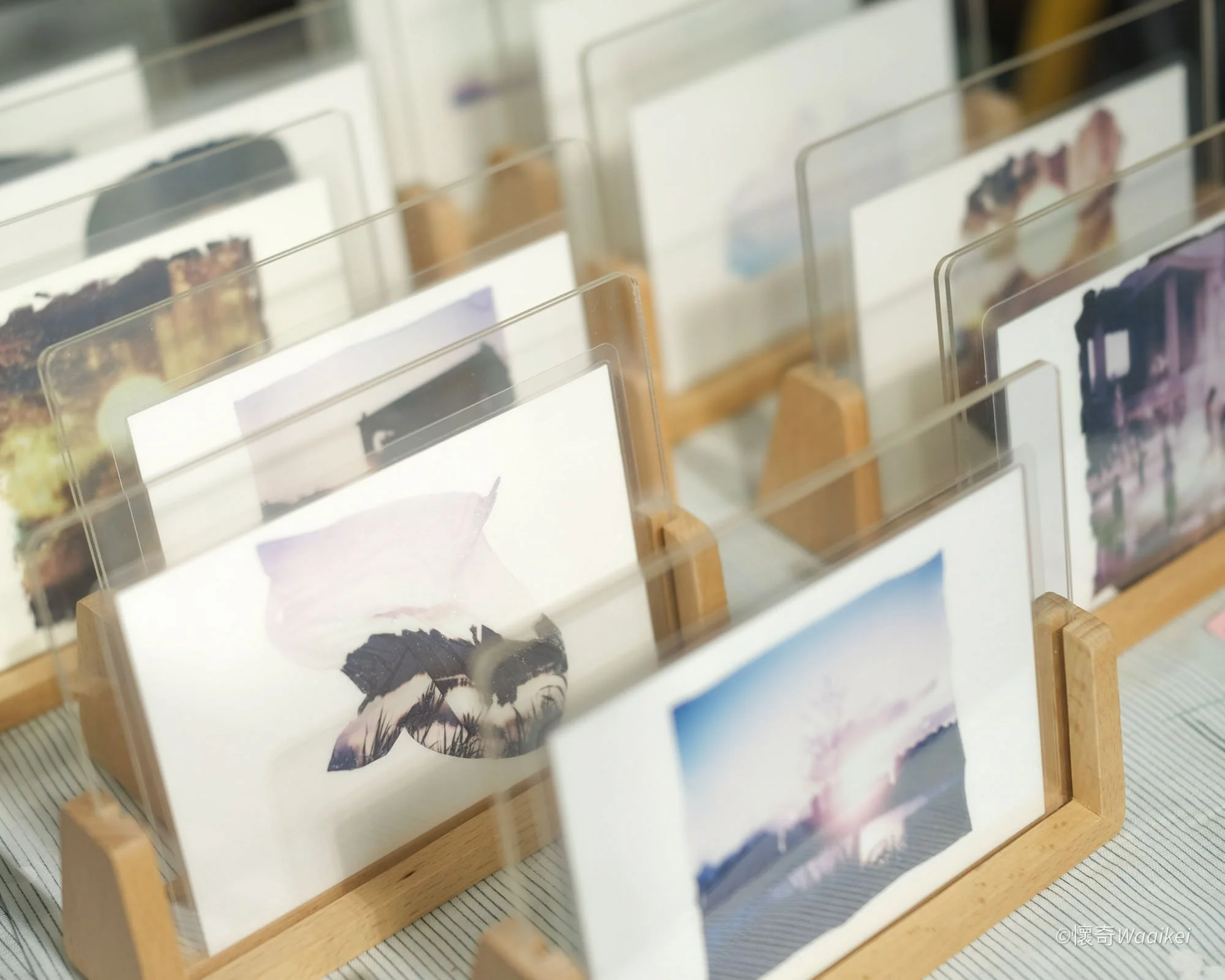 Multiple postcards with images of landscapes and portraits are displayed on a wooden stand.