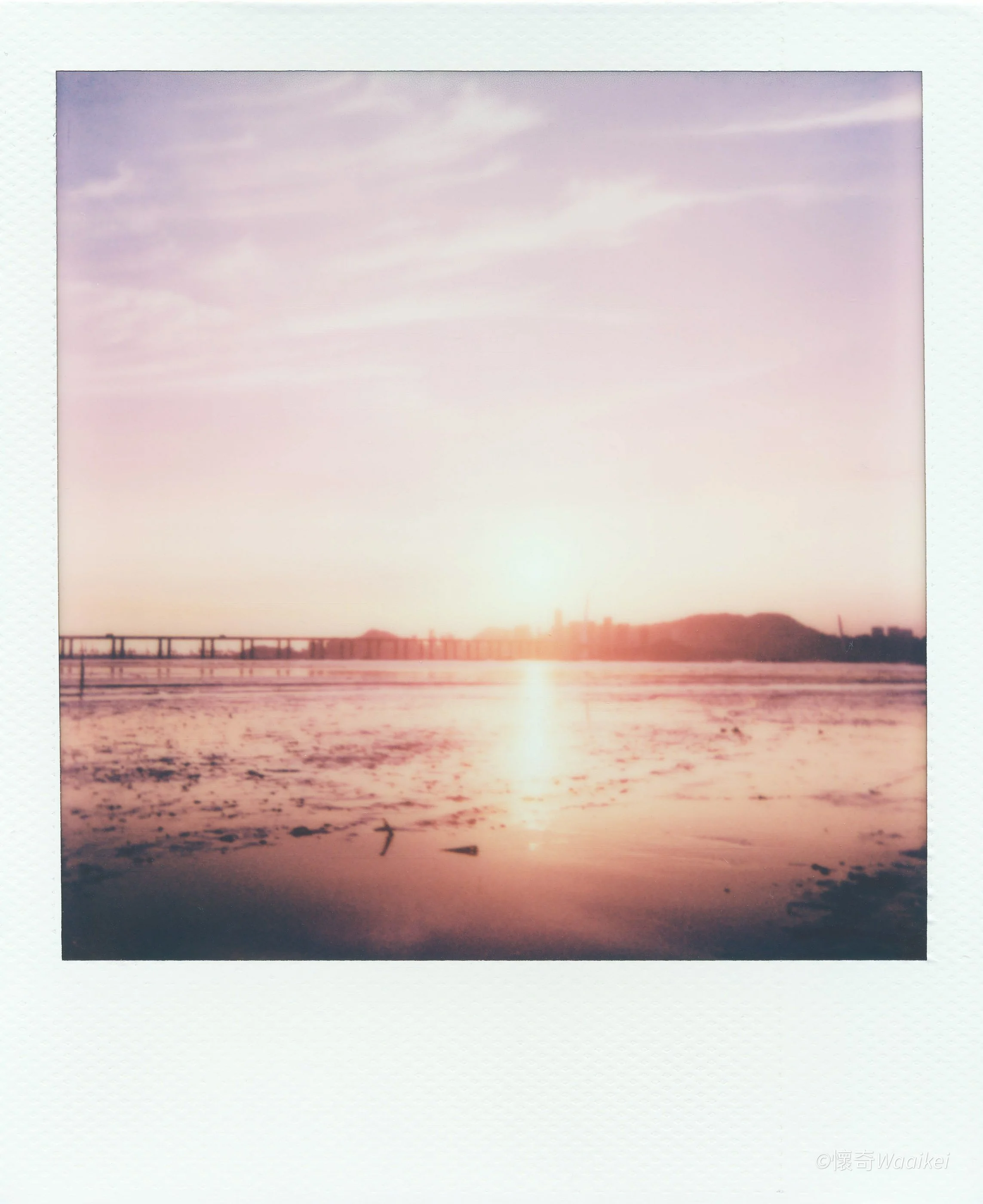 Photograph of a sunset over a body of water with a mountain in the background and a pier on the left side.