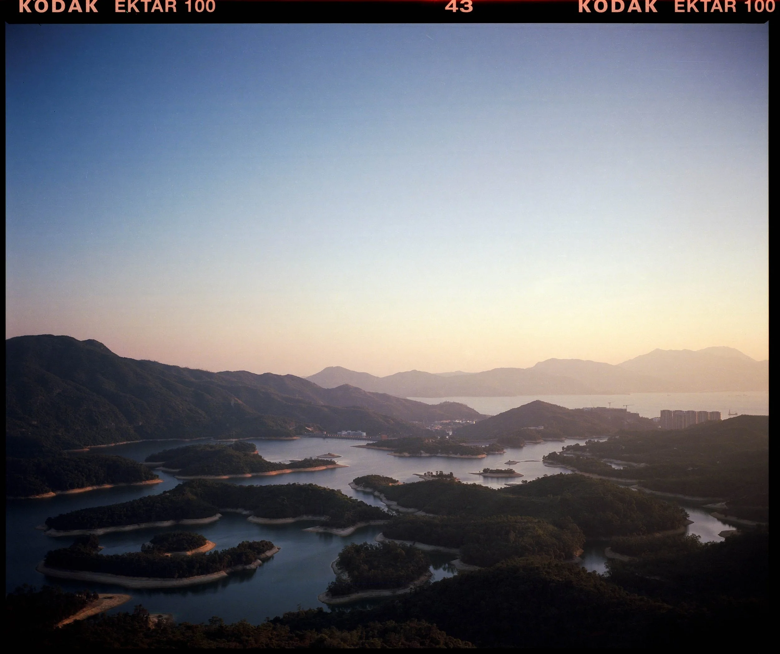 Scenic view of a large reservoir with multiple inlets and islands surrounded by green mountains during dusk or dawn.