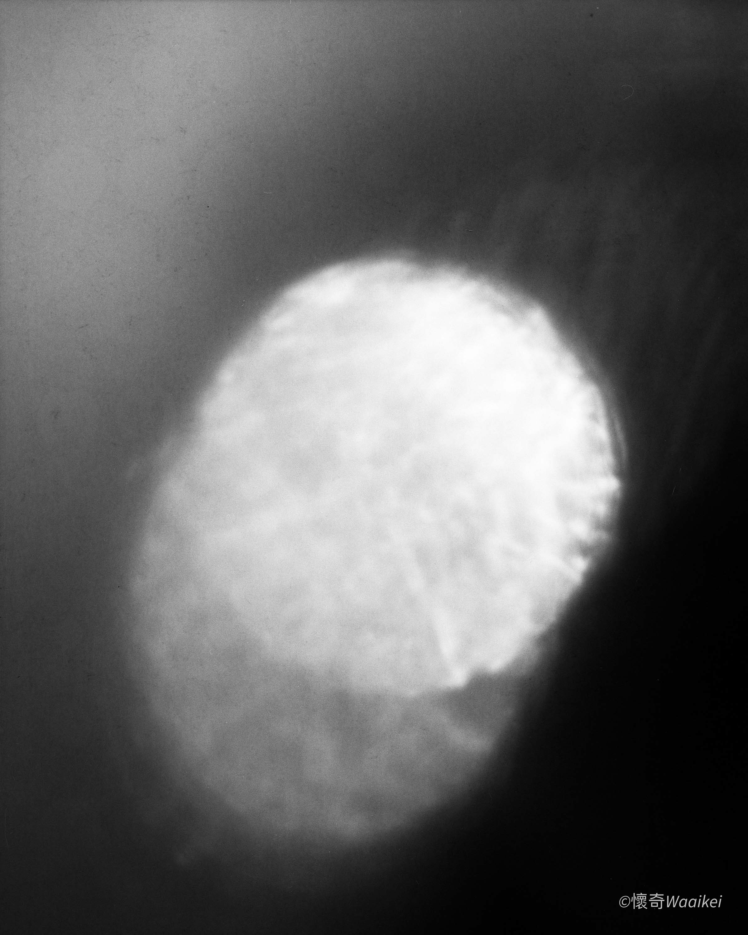 A black and white photograph of the surface of the moon, showing a crater with a rim lit by sunlight.