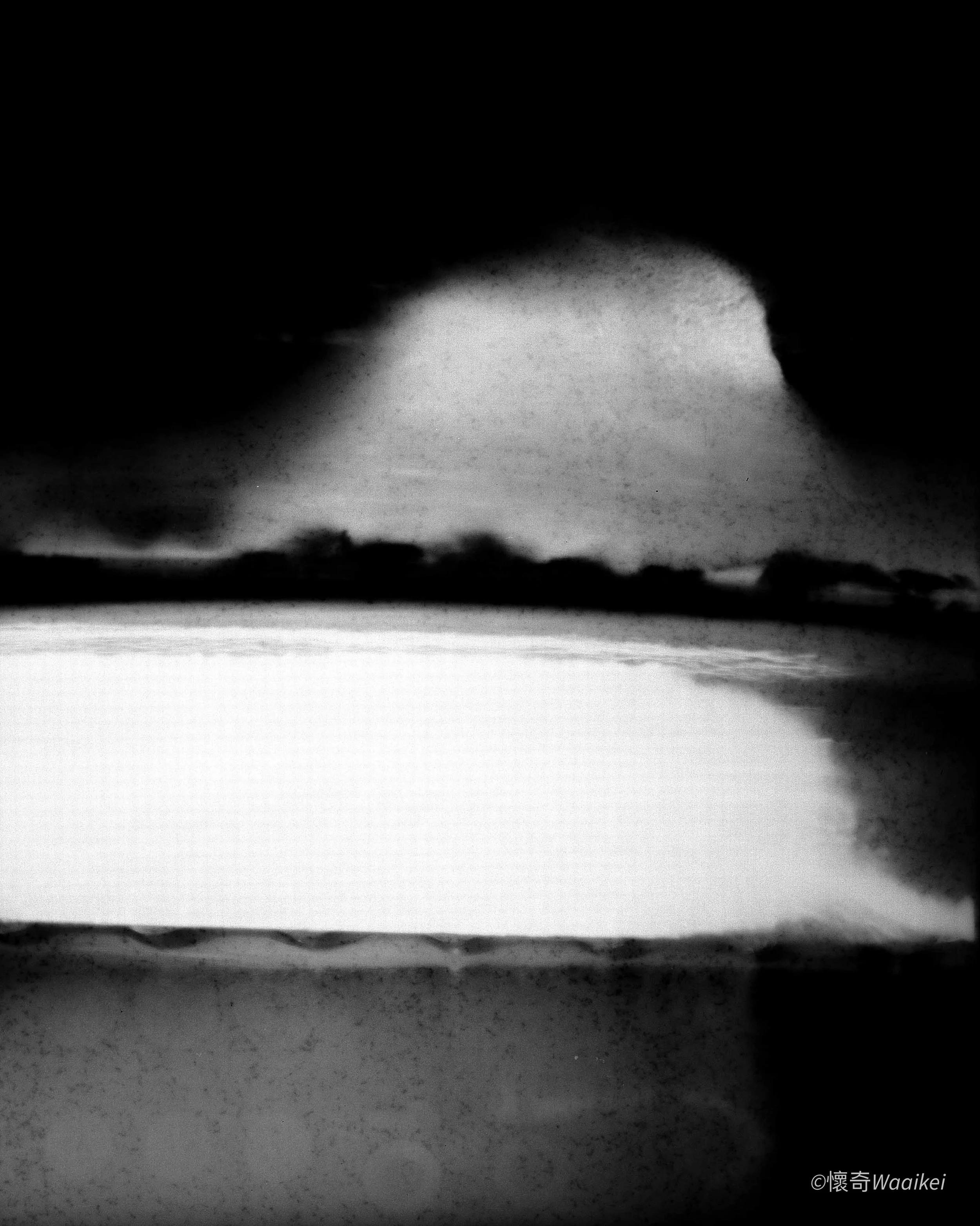A black and white photograph of a mountain partially obscured by dark clouds, with a snow-covered foreground.