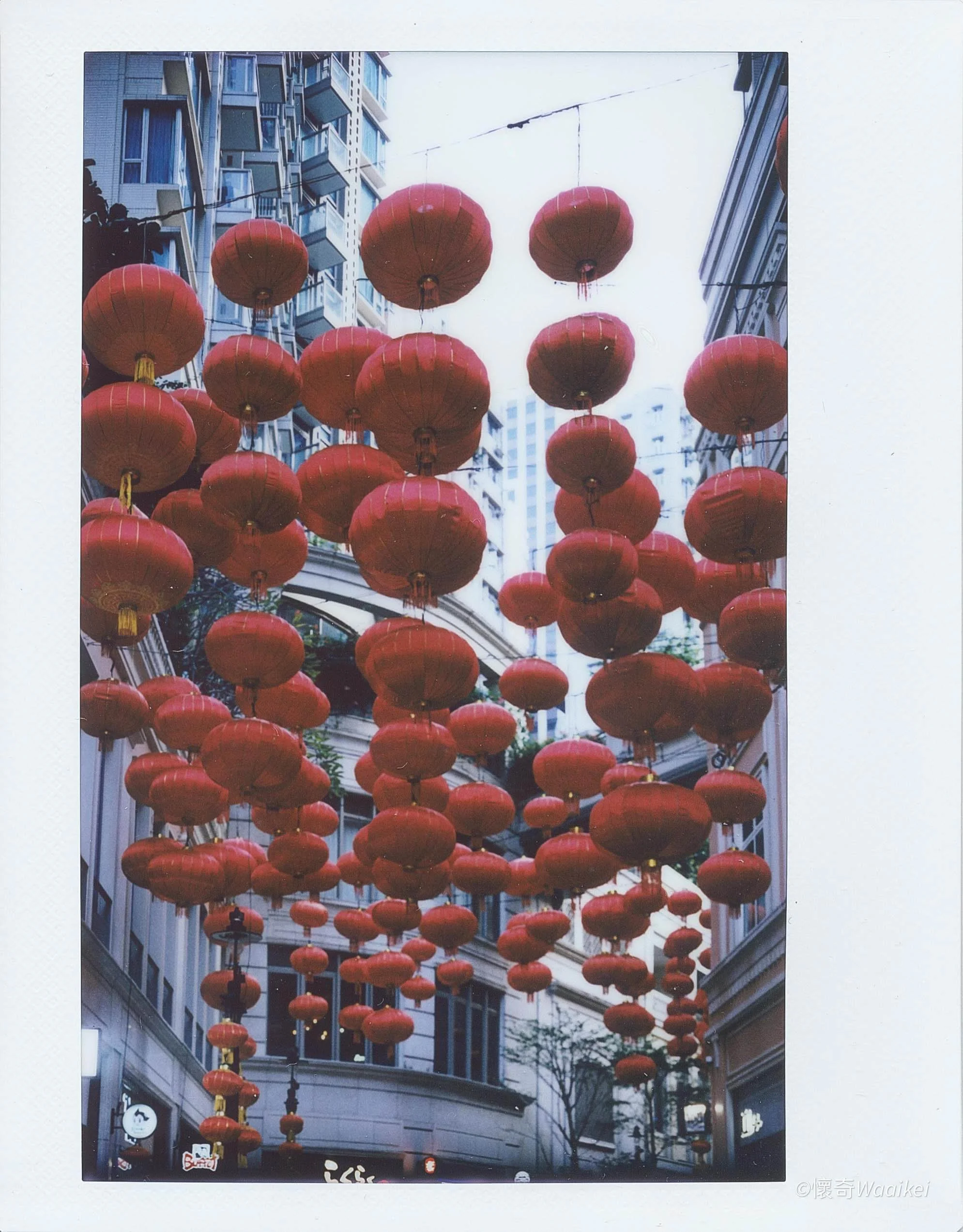 Street decorated with numerous red Chinese lanterns hanging overhead between building across a city street.