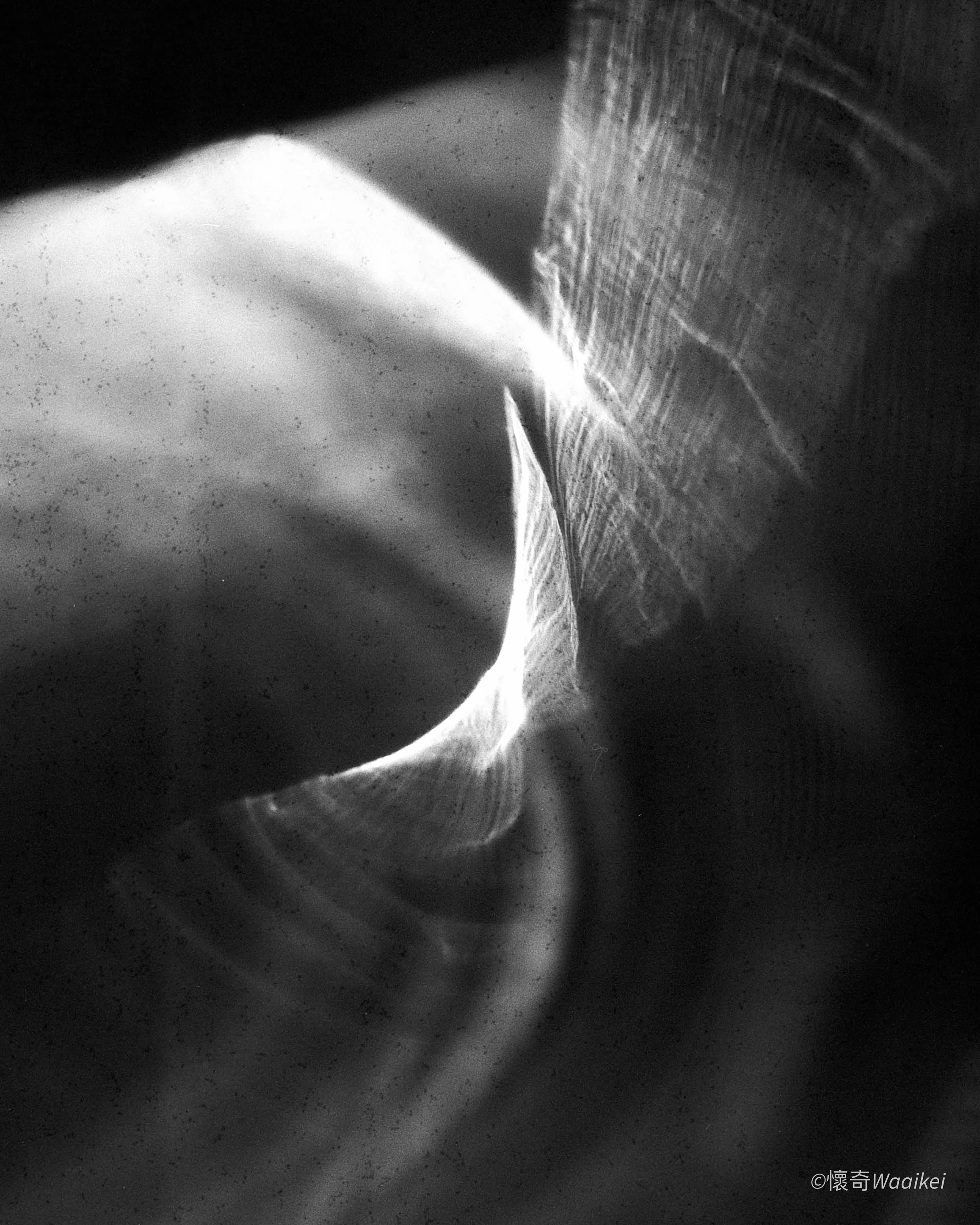 Black and white close-up photo of a bright light source creating a sharp contrast and abstract patterns on a textured surface.