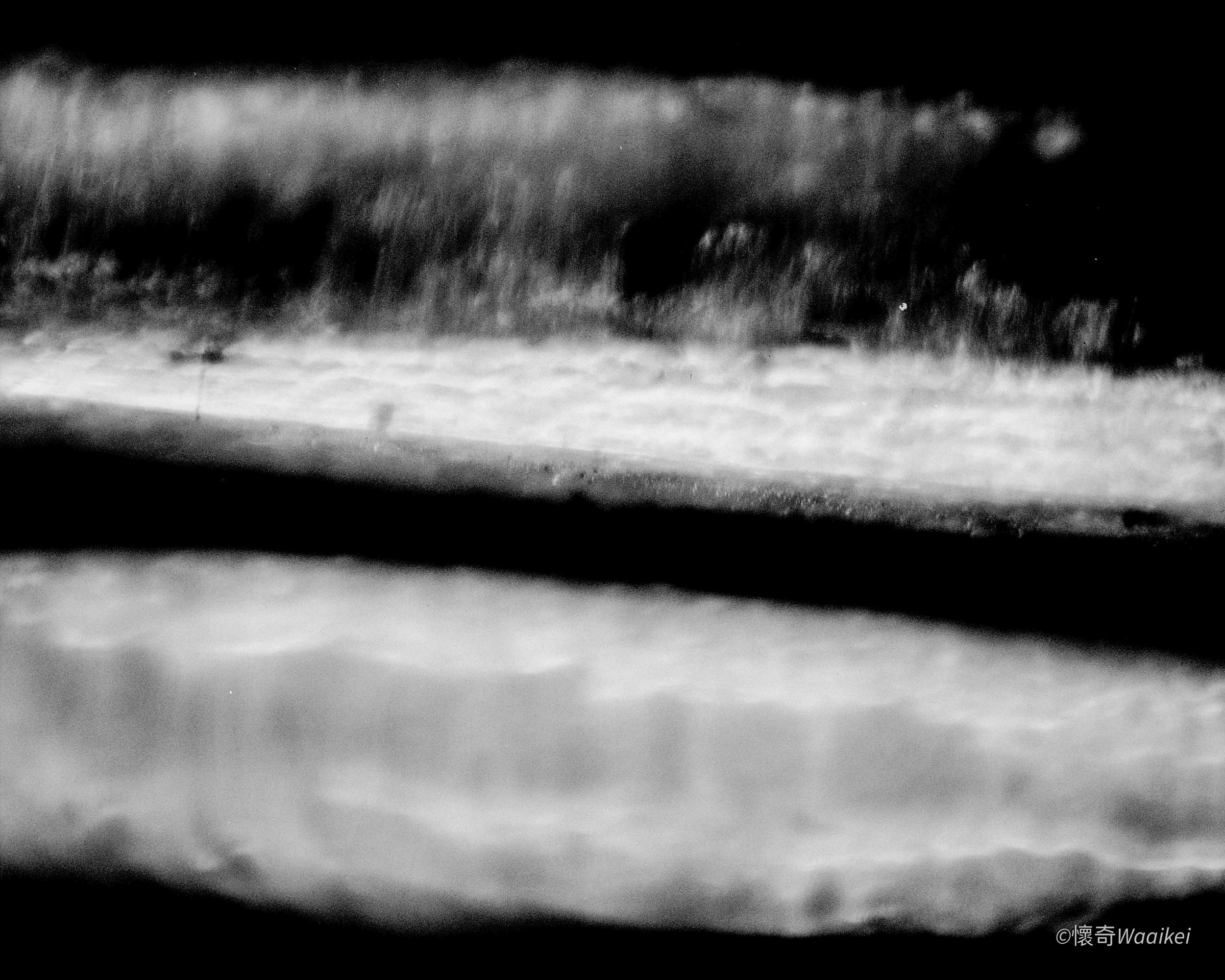 A black and white image showing a distant view of mountains or hills with clouds or fog in the sky, possibly taken from a moving vehicle.