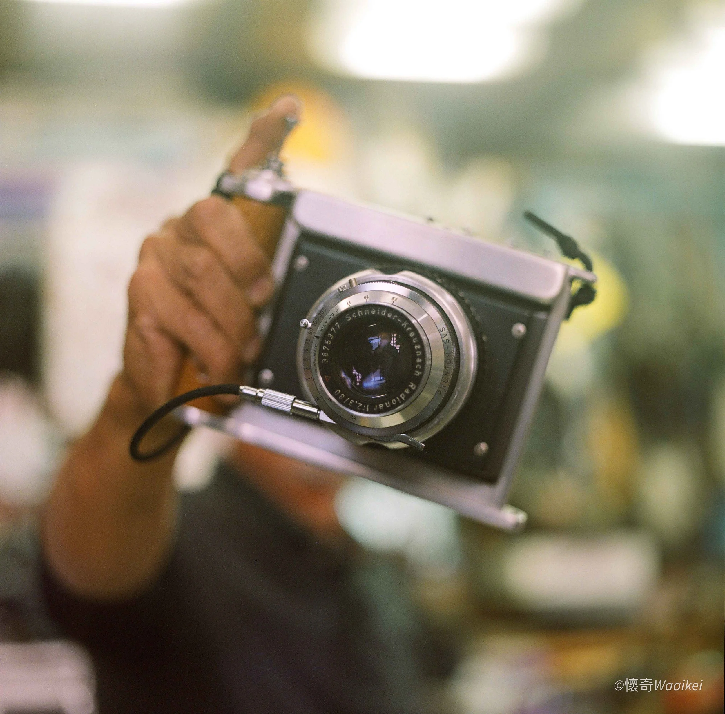 A blurry photo of a person holding a vintage camera, with a bright light source in the background