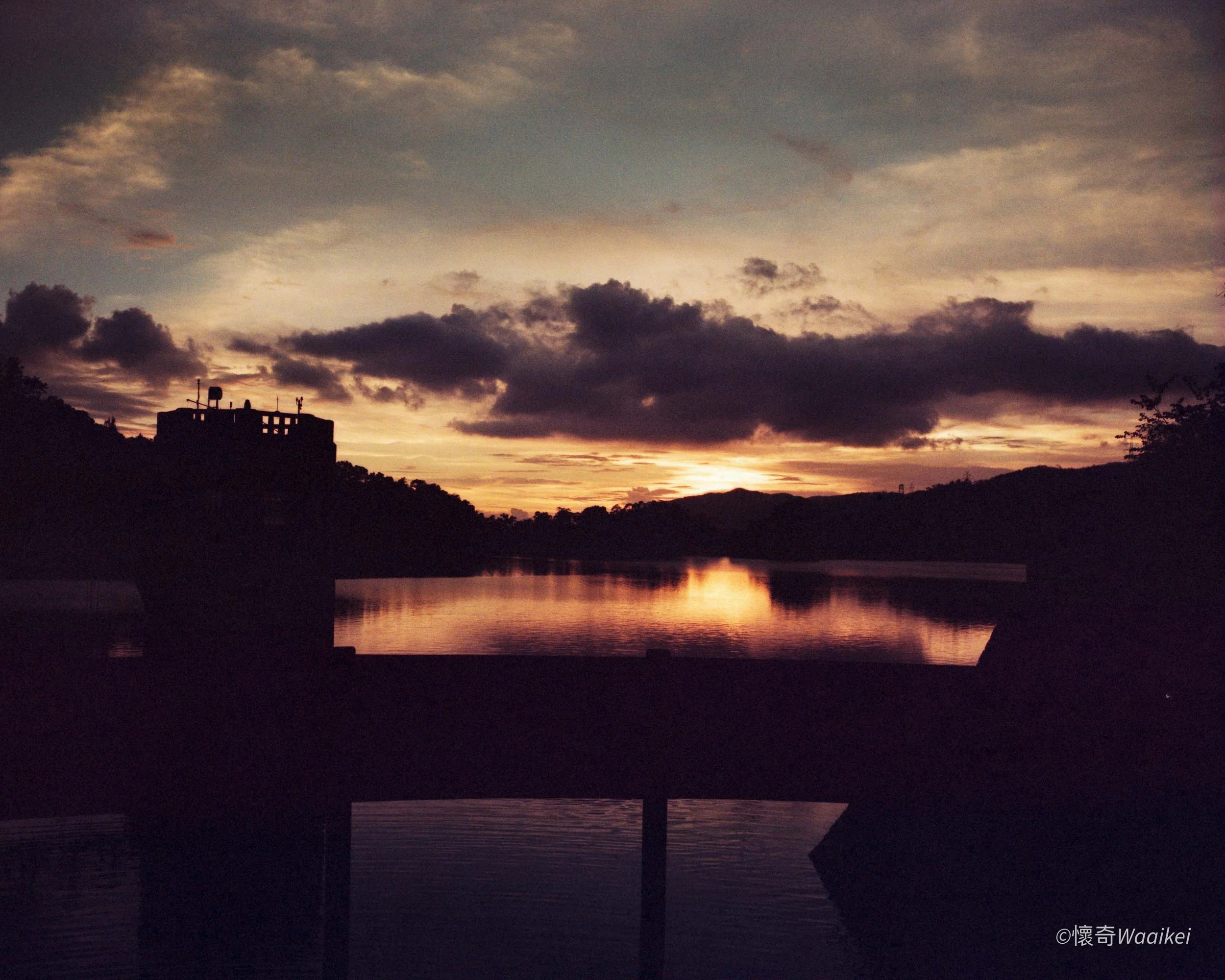 A sunset over a body of water with silhouetted trees and clouds in the sky.