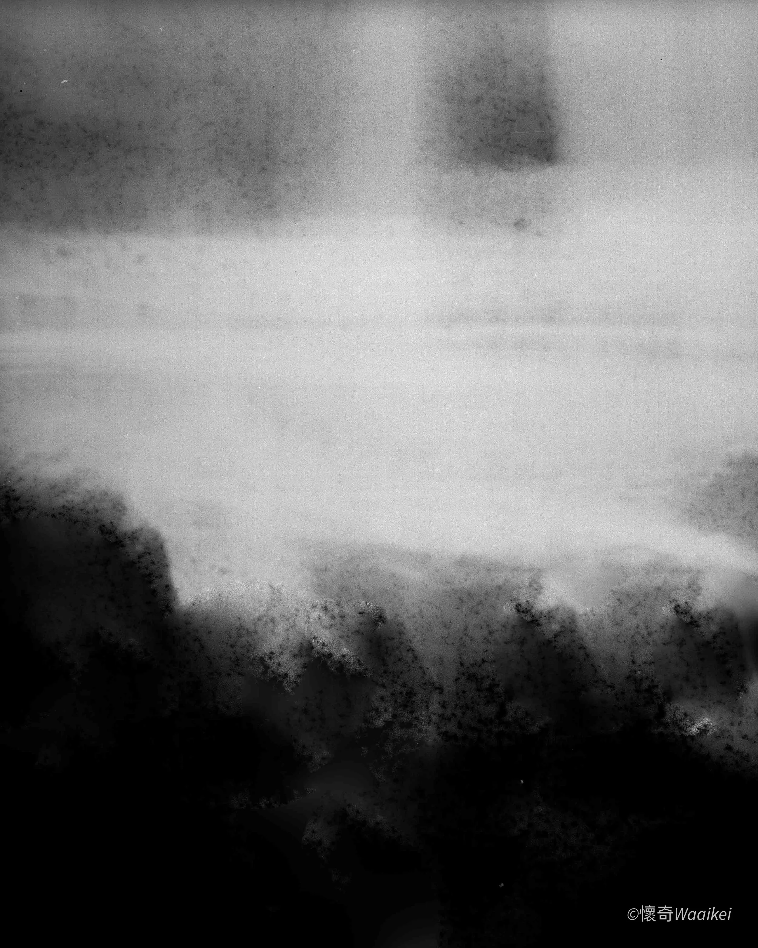 Black and white photograph of a landscape with dark clouds in the sky, a horizon, and a shadowy foreground with some textured elements.