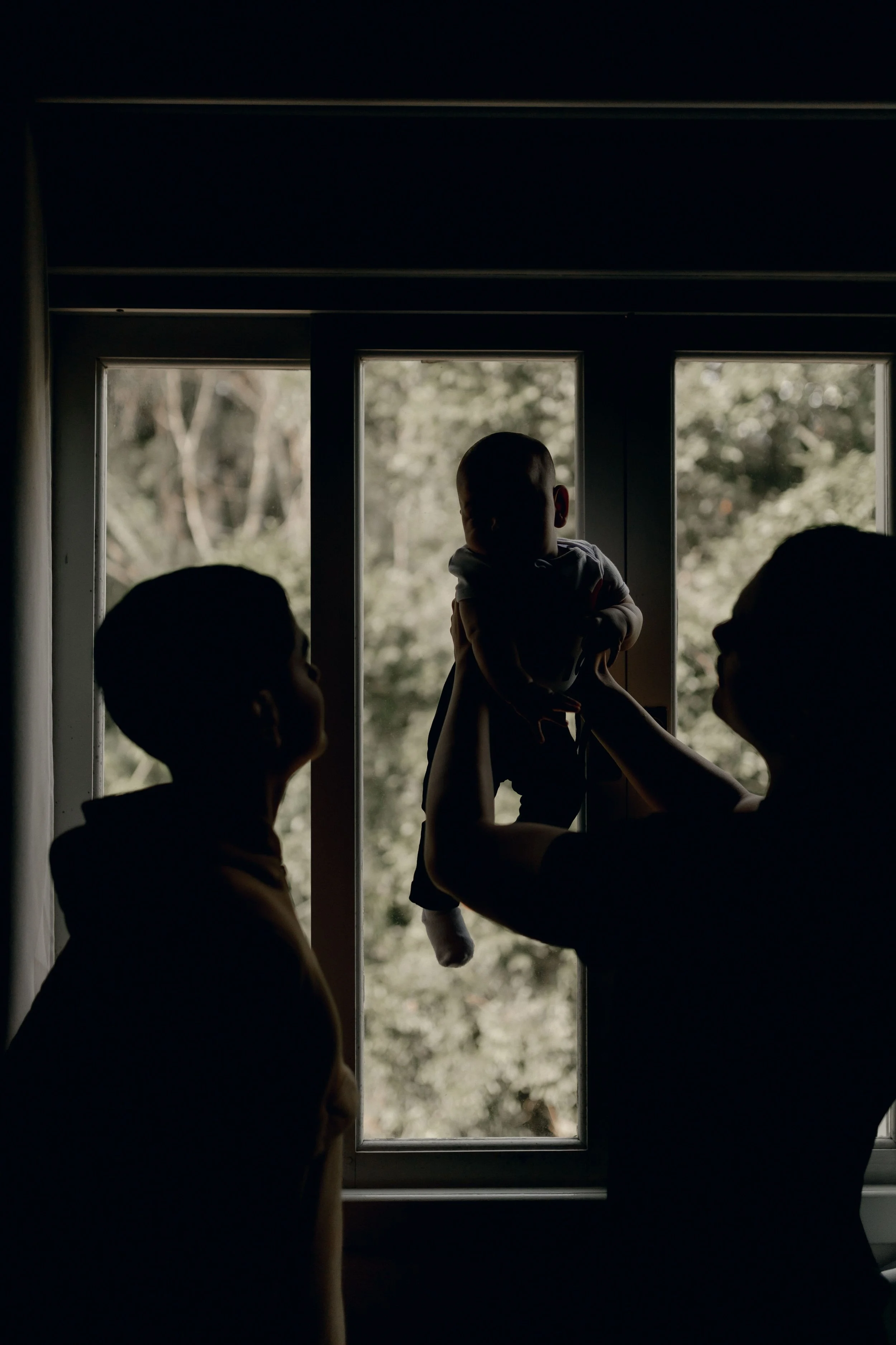 Parents holding their baby together near a sunlit window