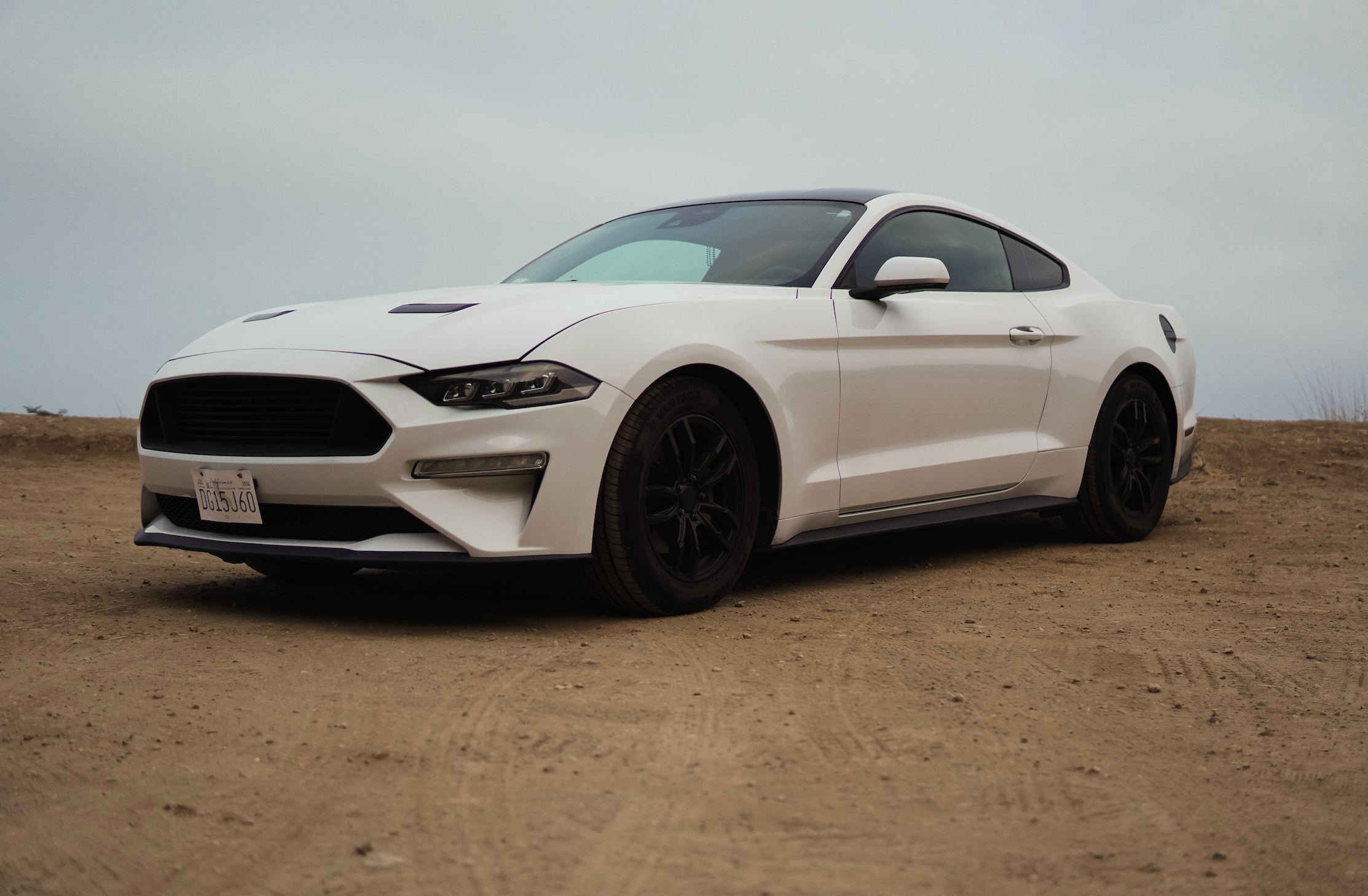 A white modern sports coupe car parked on a dirt surface with a cloudy sky background.