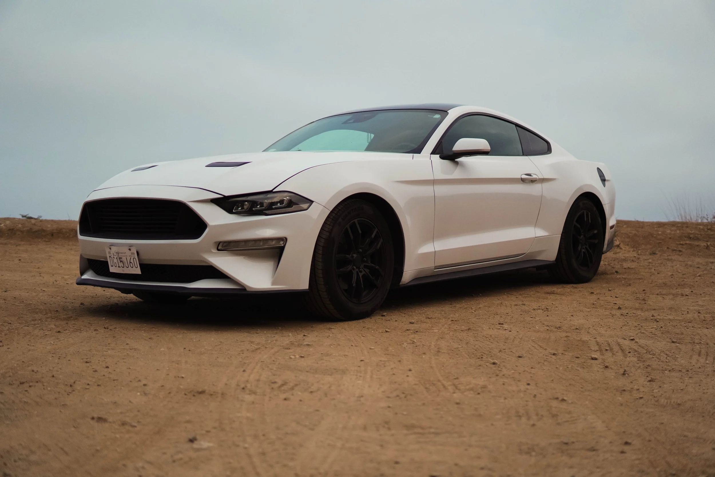 A white sports car with a sleek, modern design parked on a dirt ground under a cloudy sky.