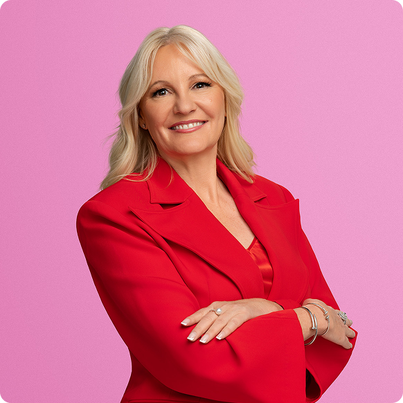 A smiling woman with blonde hair wearing a red blazer against a pink background.