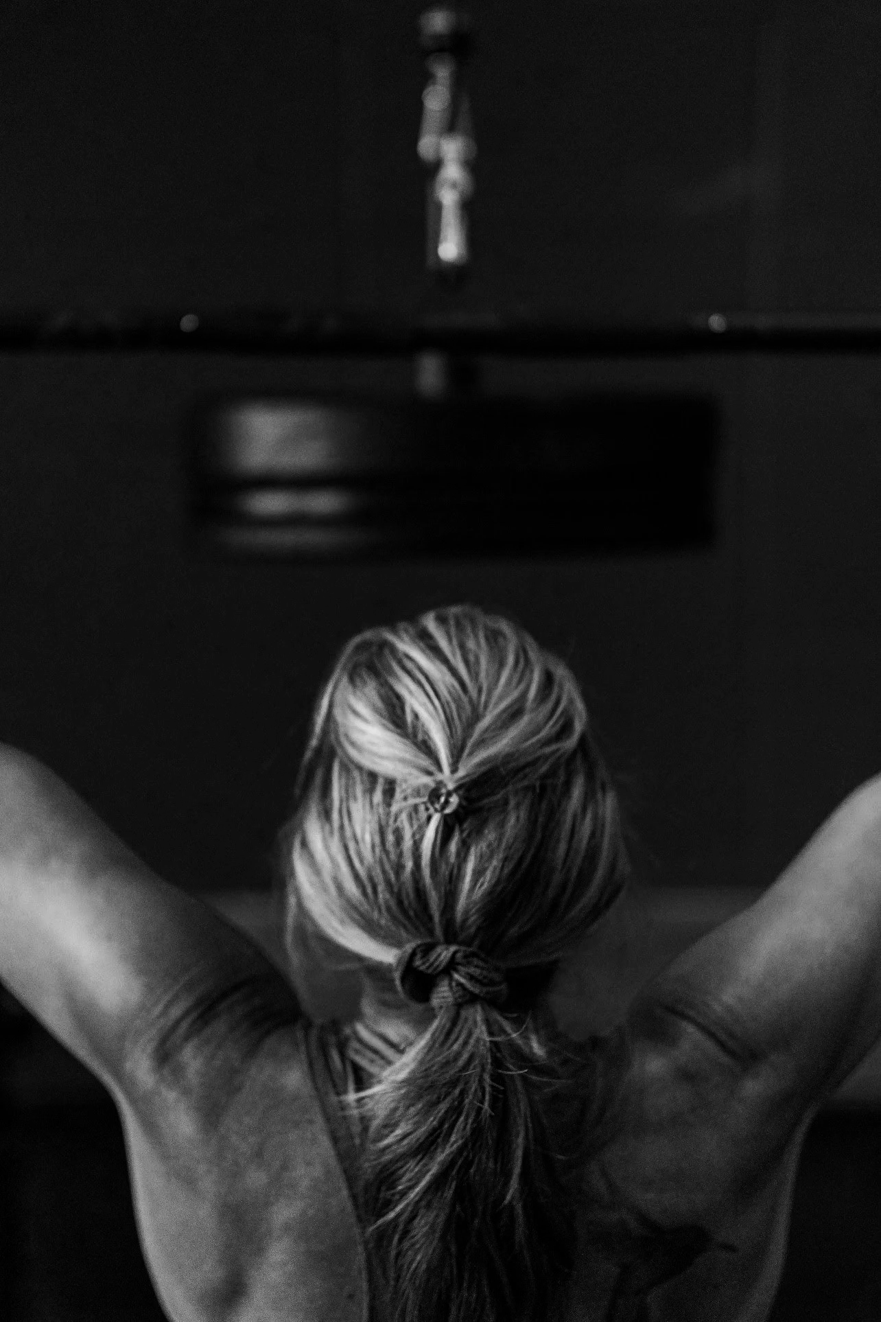 back of womans head with her arms up pulling down weight