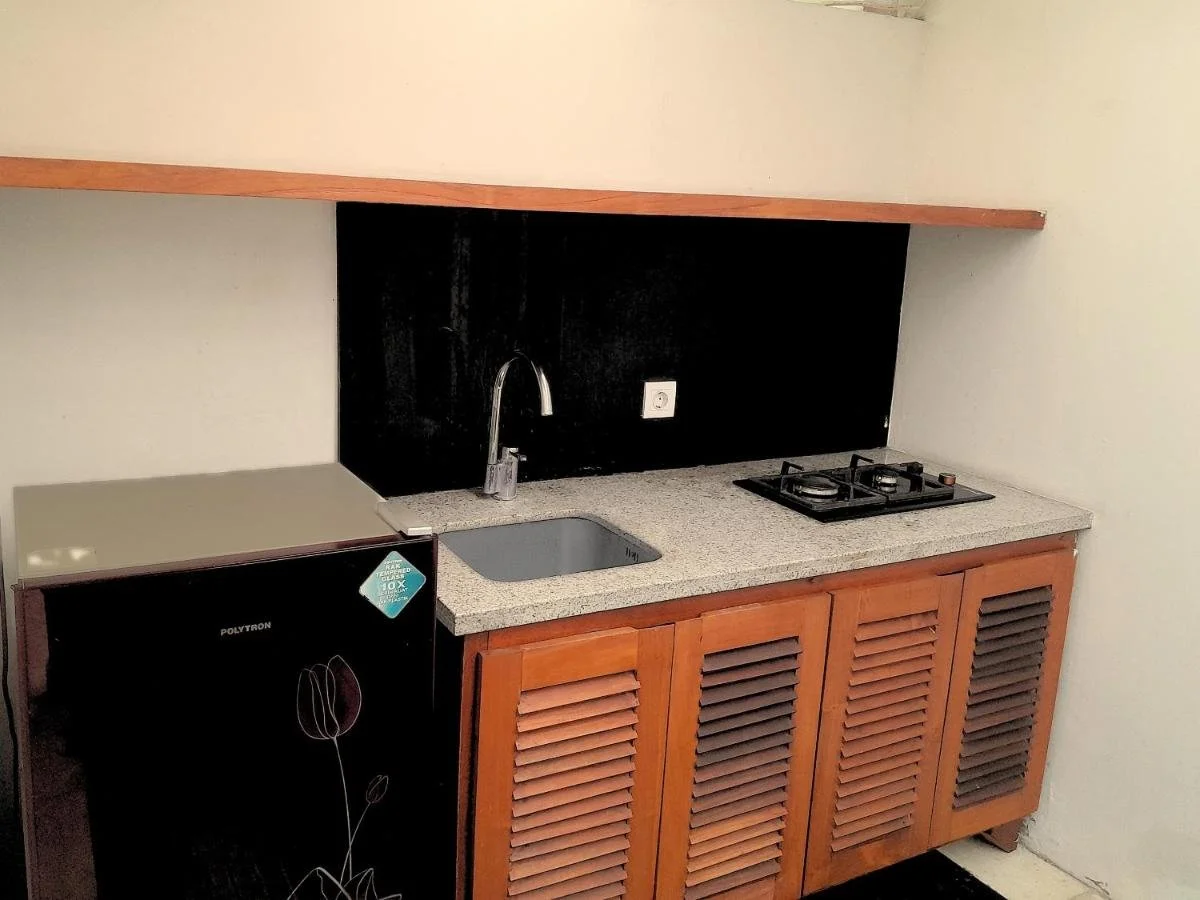 A small kitchen area with a mini refrigerator, a countertop with a sink, and a two-burner stove, featuring wooden cabinet doors below and a black backsplash behind the sink and stove.