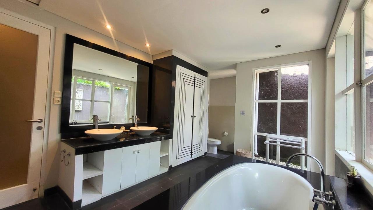 Modern bathroom with a double vanity featuring two vessel sinks, a large mirror, a white toilet, a bathtub, and large windows providing natural light.