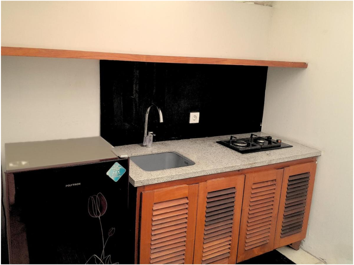 A small kitchen area with a mini refrigerator, a countertop with a sink, and a two-burner stove, featuring wooden cabinet doors below and a black backsplash behind the sink and stove.