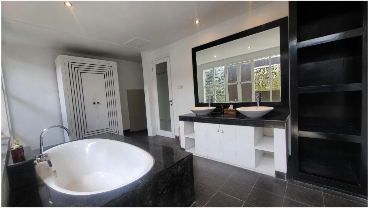 Modern bathroom with black and white color scheme, double vanity with vessel sinks, large mirror, black shelving unit, bathtub, and window overlooking greenery.