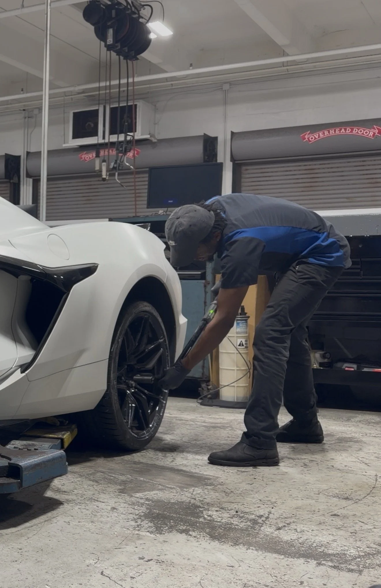 Person working on a white sports car in an indoor garage or workshop.