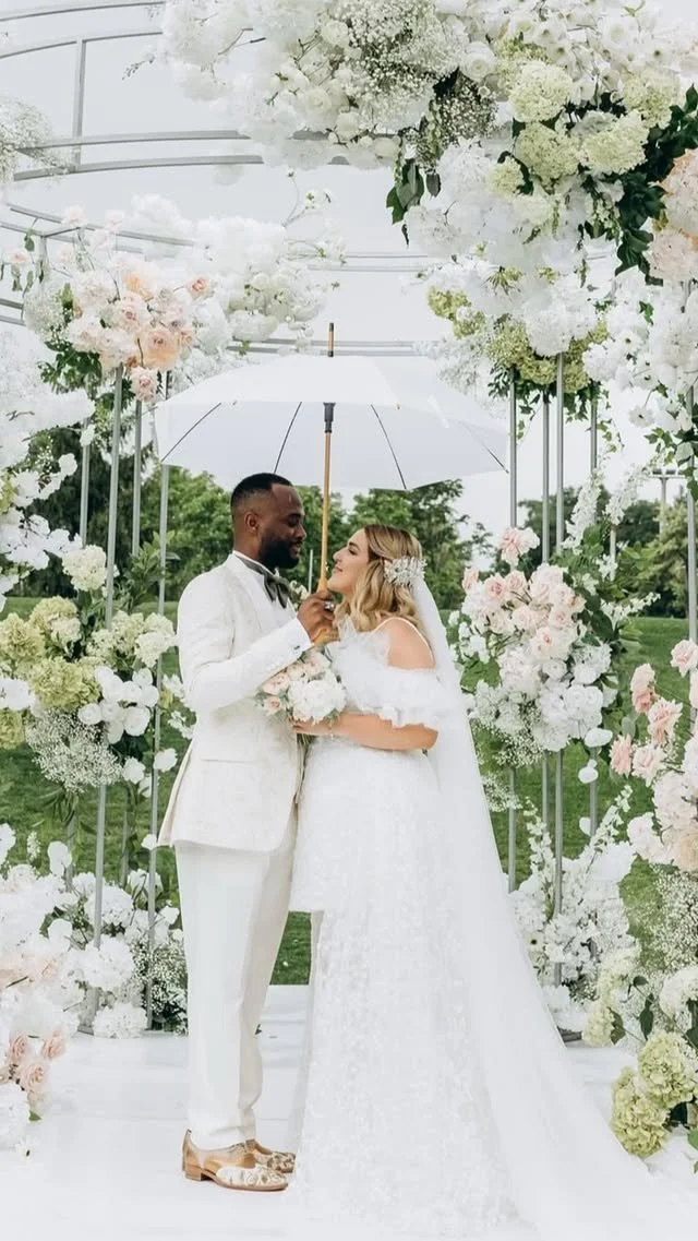 A wedding ceremony with a couple holding an umbrella surrounded by white and light pink flowers.