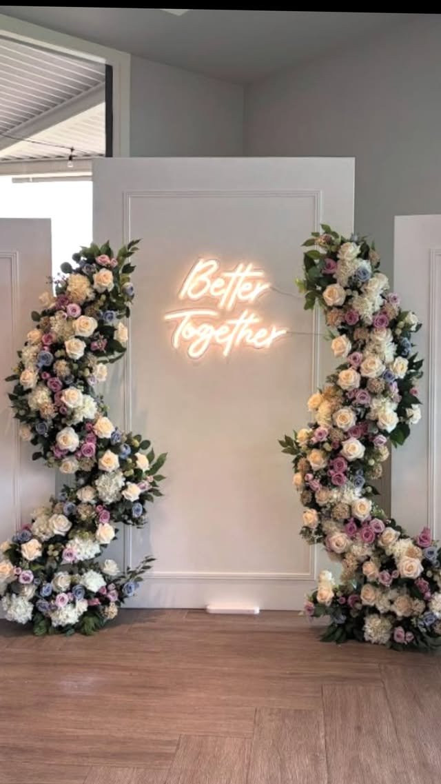 Floral arrangement on both sides of a white panel with a neon sign reading "Better Together" in cursive