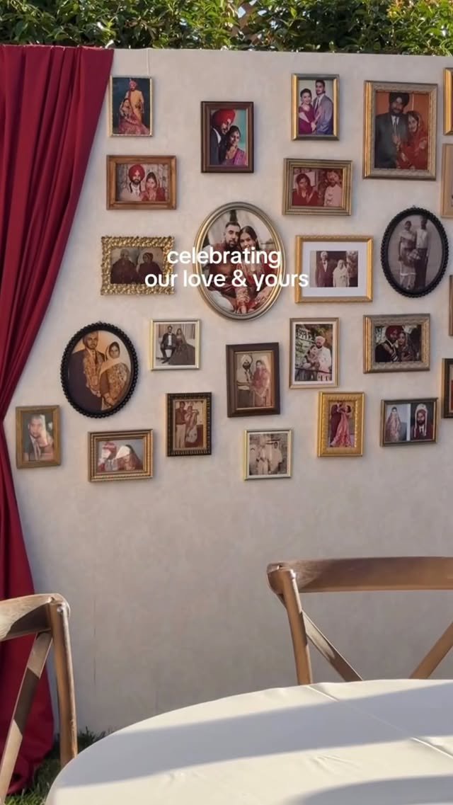 Wall decorated with numerous framed family photos, some in black-and-white and color, with a text overlay saying "celebrating our love & yours." There is a red curtain on the left side and part of a table with chairs in the foreground.