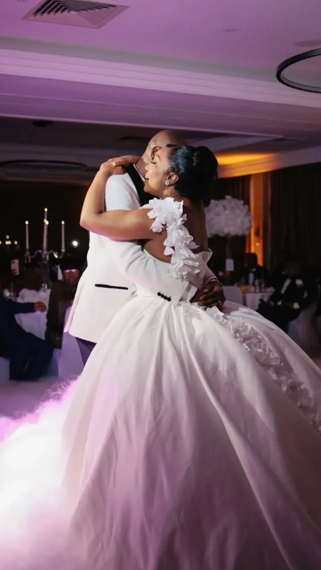 A bride and groom sharing a dance at their wedding reception, with guests seated in the background.