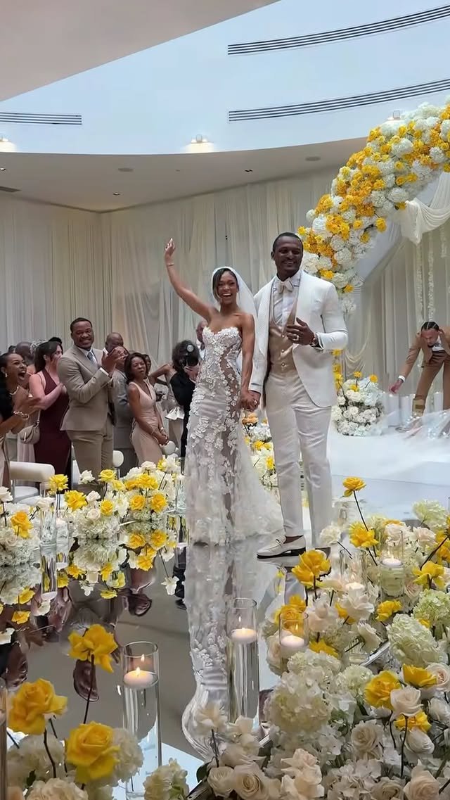 Bride and groom standing at the altar during their wedding ceremony, surrounded by floral arrangements and guests celebrating.