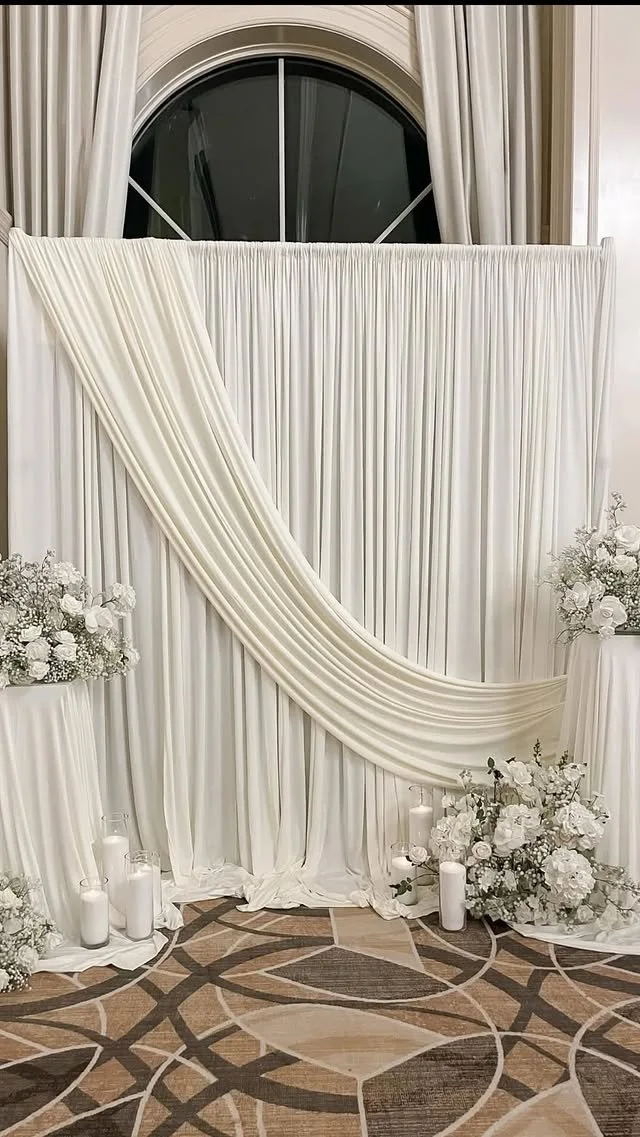 Elegant wedding backdrop with white drapery, floral arrangements, and candles.