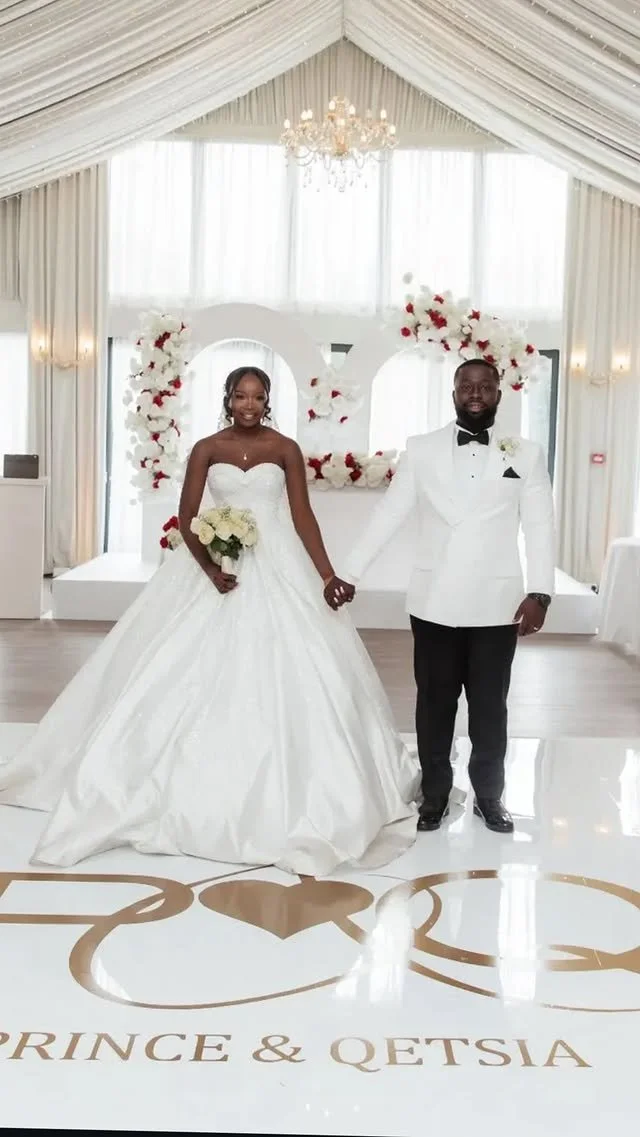 Bride and groom holding hands, standing in a wedding venue with floral decorations and elegant drapery.