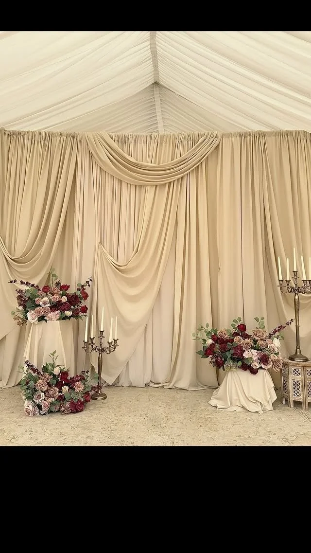 Elegant wedding ceremony backdrop with beige draped curtains, floral arrangements with roses, and tall candelabras with candles.