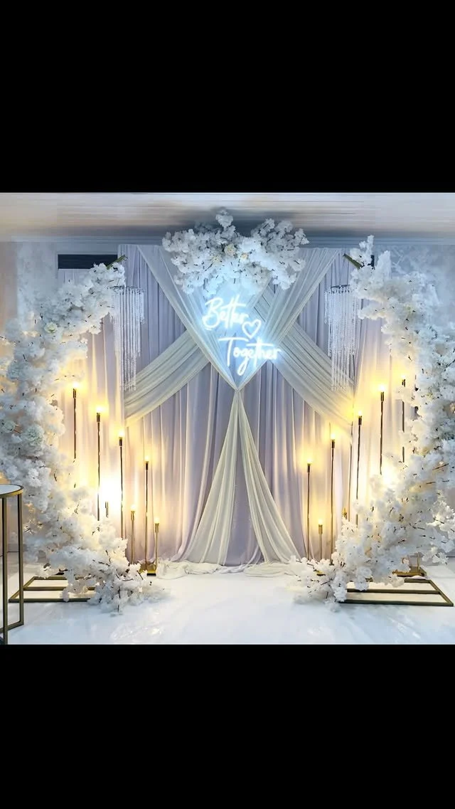 Elegant wedding backdrop with white drapes, floral arches, and glowing lights, featuring a neon sign that says 'Both Together' with a heart.