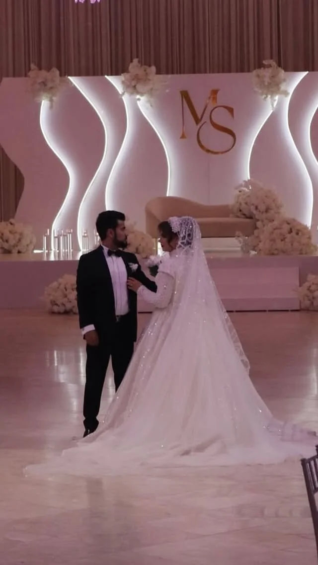 Bride and groom dancing at wedding reception with floral decorations and a large monogram backdrop 'VS'.