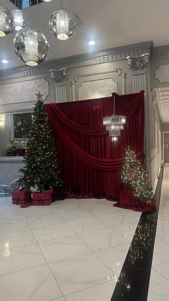 Decorative Christmas scene with two decorated Christmas trees, red draped curtains, and a crystal chandelier in an elegant room.