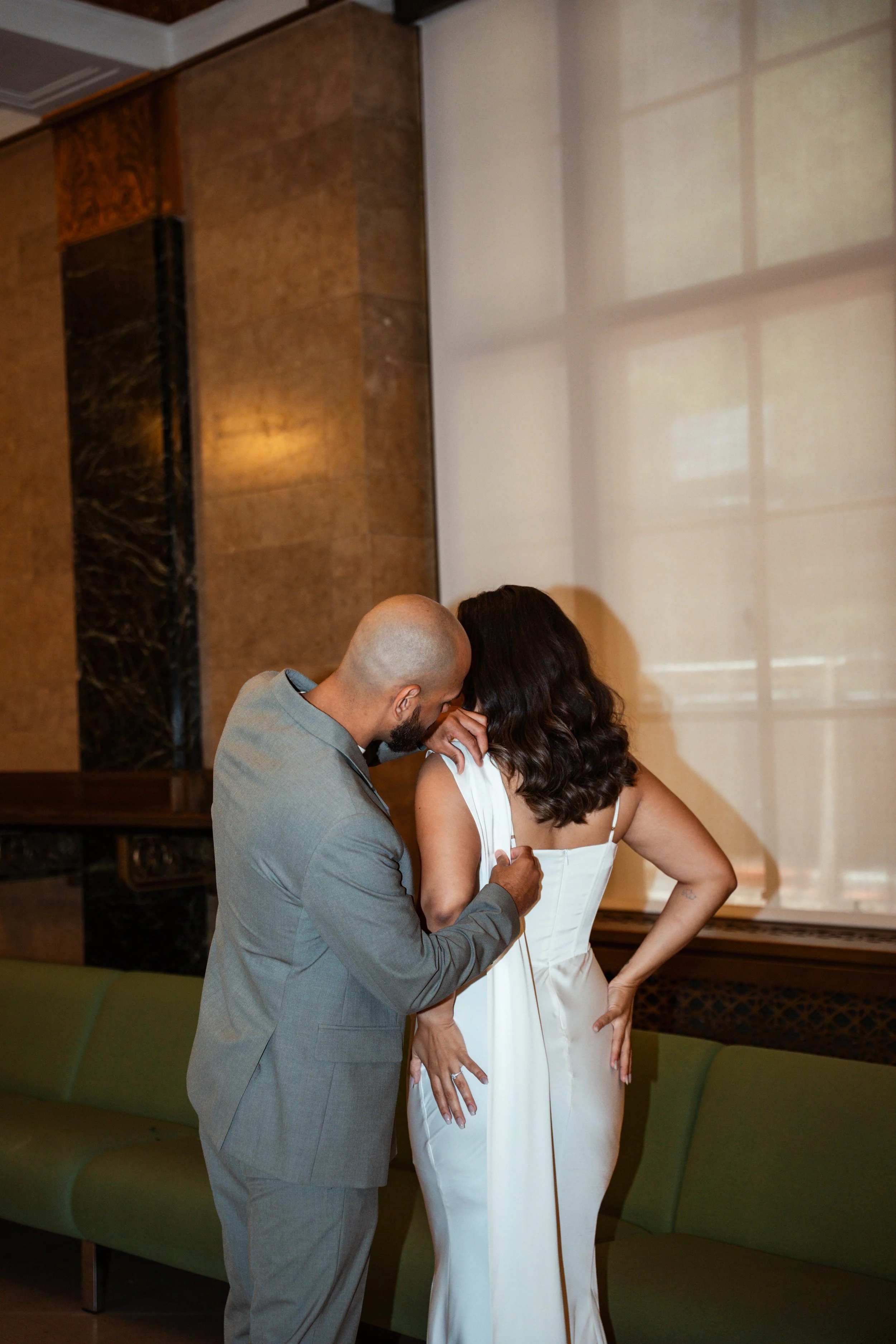 A man in a gray suit places a ring on the finger of a woman in a white dress during a wedding ceremony indoors.