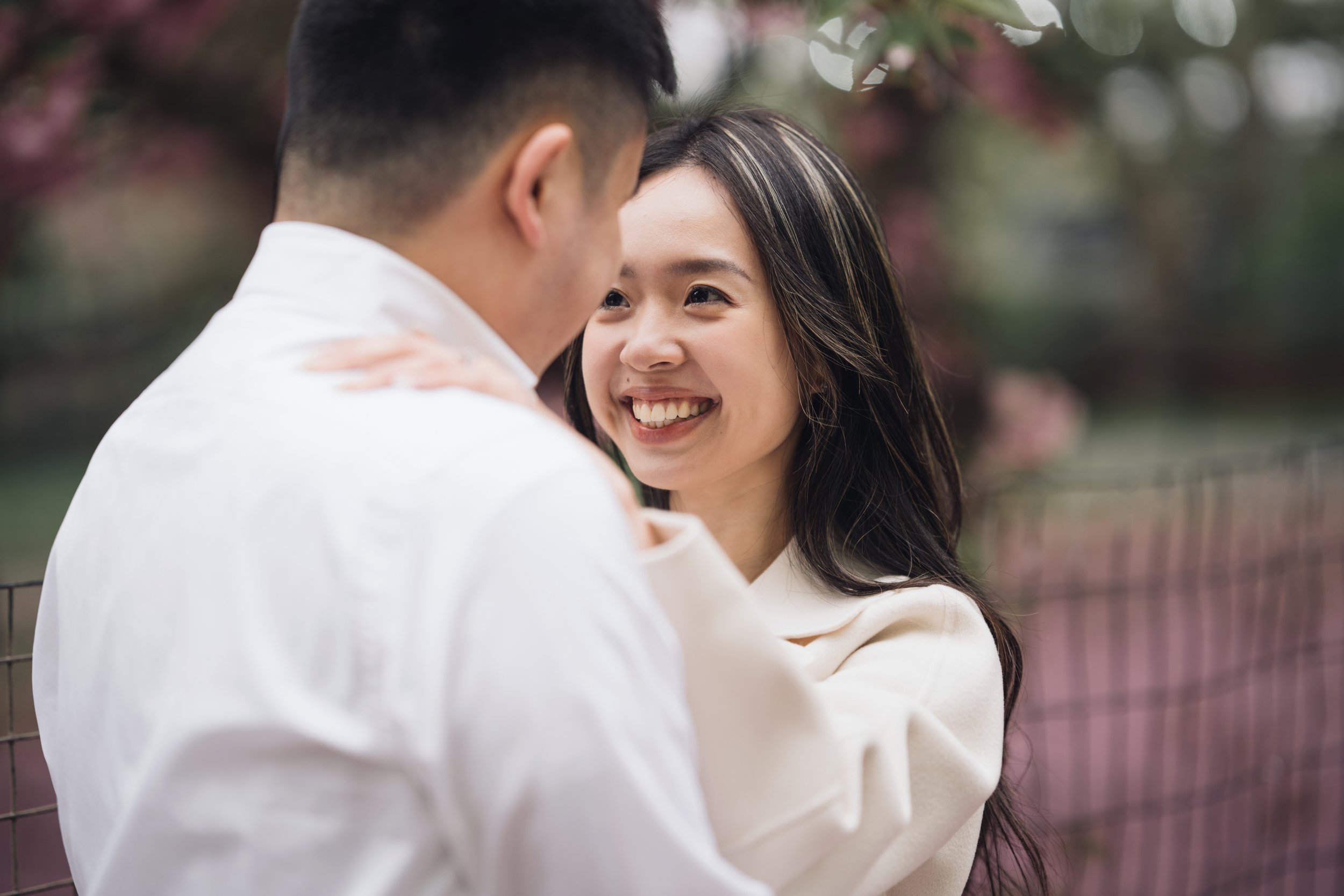 A couple sharing an intimate moment outdoors, with the woman smiling and the man gently leaning in.