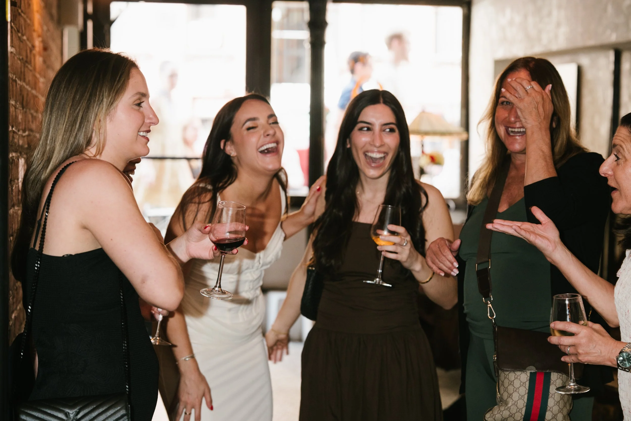 A group of women enjoying conversation and laughter at a social gathering, holding glasses of wine.