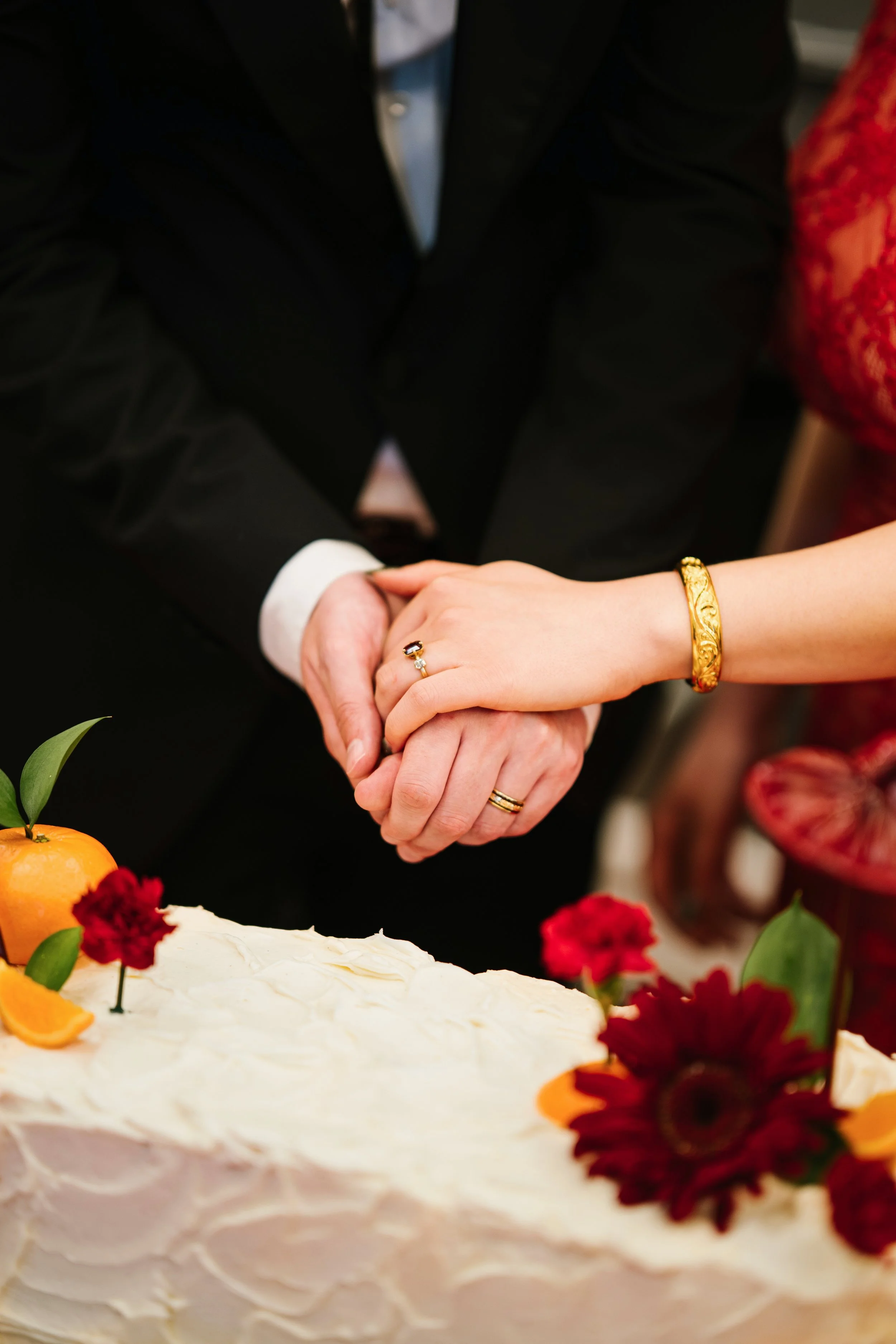 Close-up of a couple holding hands over a wedding cake decorated with fruit and flowers.